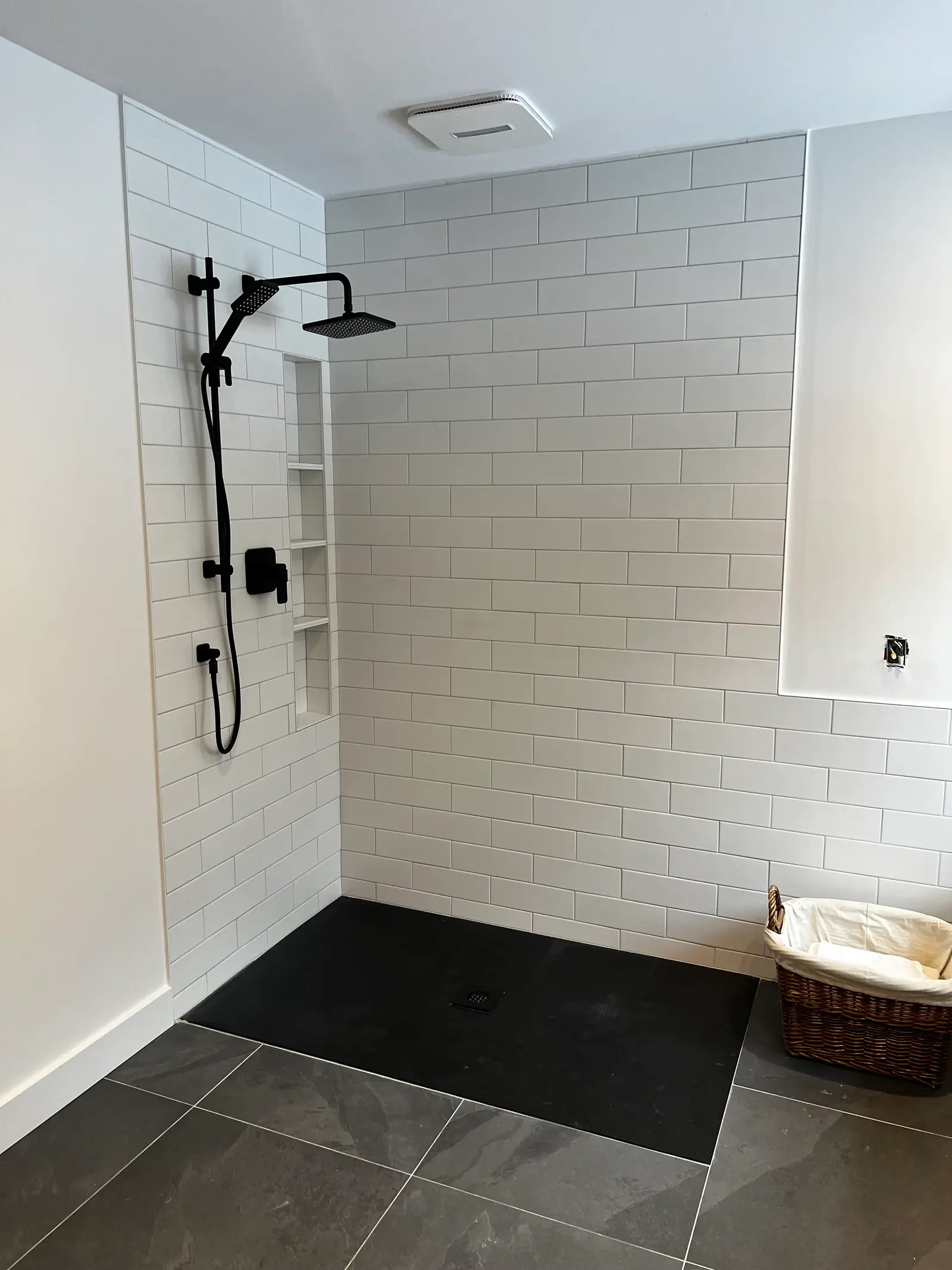 Douche italienne moderne avec carrelage métro blanc, robinetterie noire, niche murale et plancher foncé
