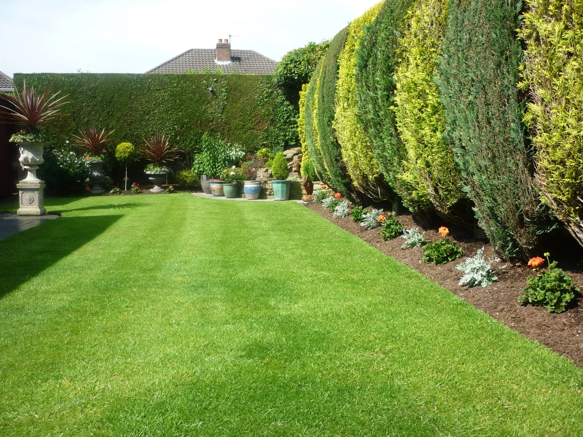 Well-maintained residential garden with green lawn, trimmed hedges, and decorative flower pots 