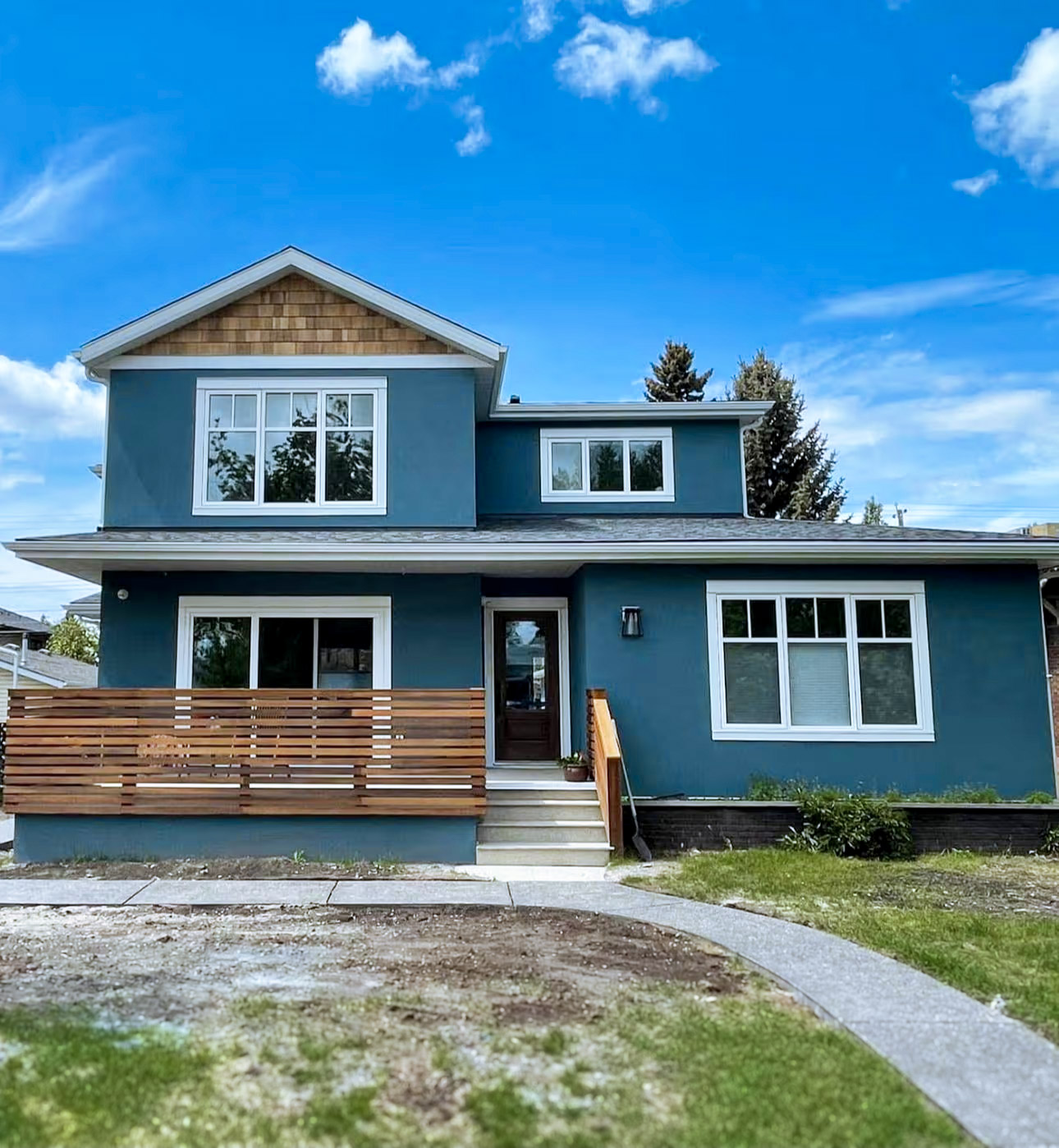 Maison moderne bleue avec revêtement extérieur uniforme, accents de bois en pignon et balcon avec garde-corps en bois