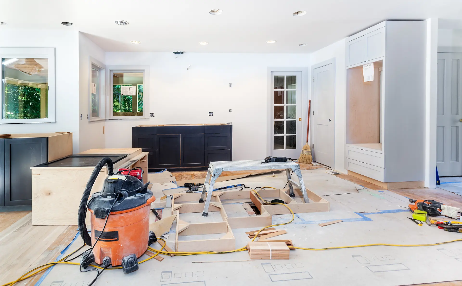 Kitchen under renovation with cabinet installation, construction tools, and flooring in progress.
