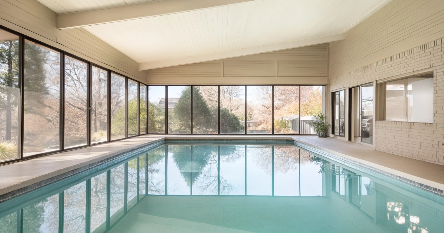 Bright indoor pool surrounded by large floor-to-ceiling windows with sloped ceiling and light brick walls