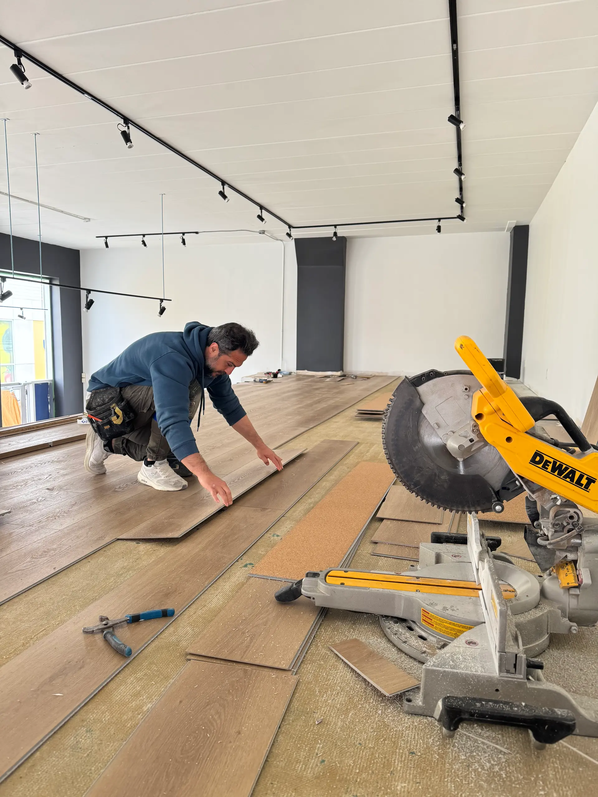 Laminate flooring installation in a renovated commercial space with miter saw and installer at work