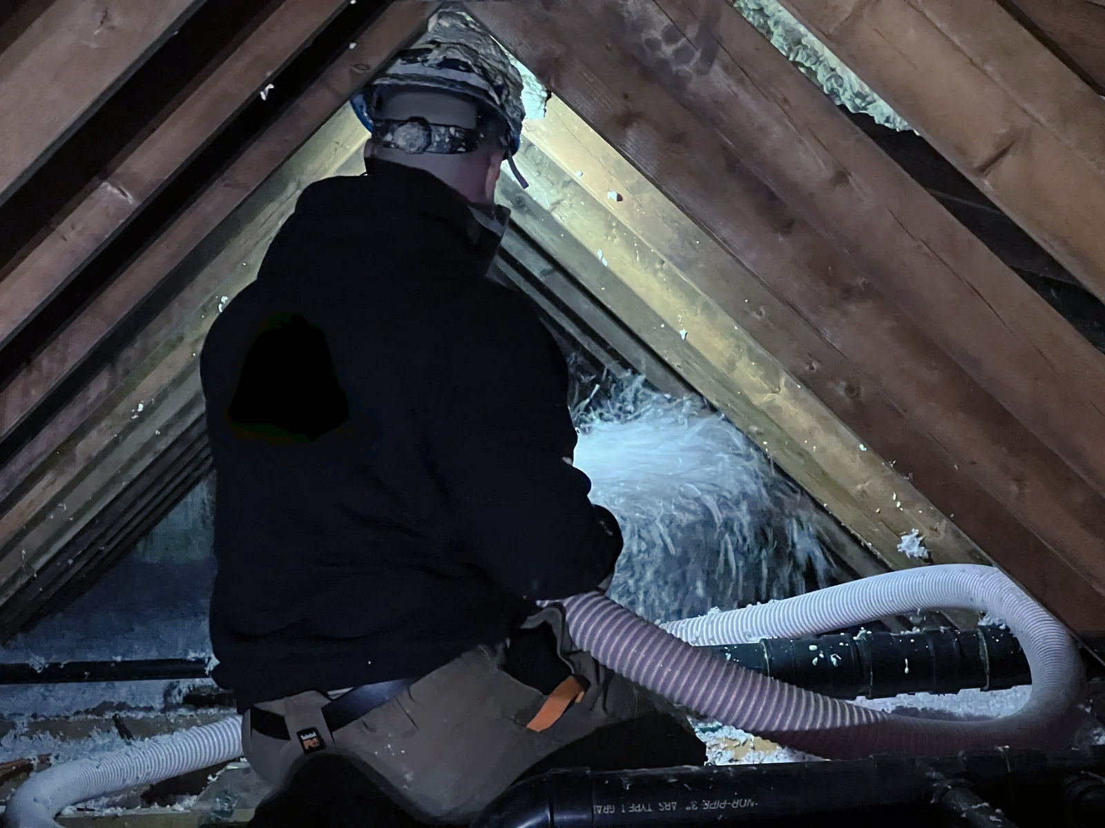 Worker blowing loose-fill insulation into a dark attic using a flexible hose to improve energy efficiency.
