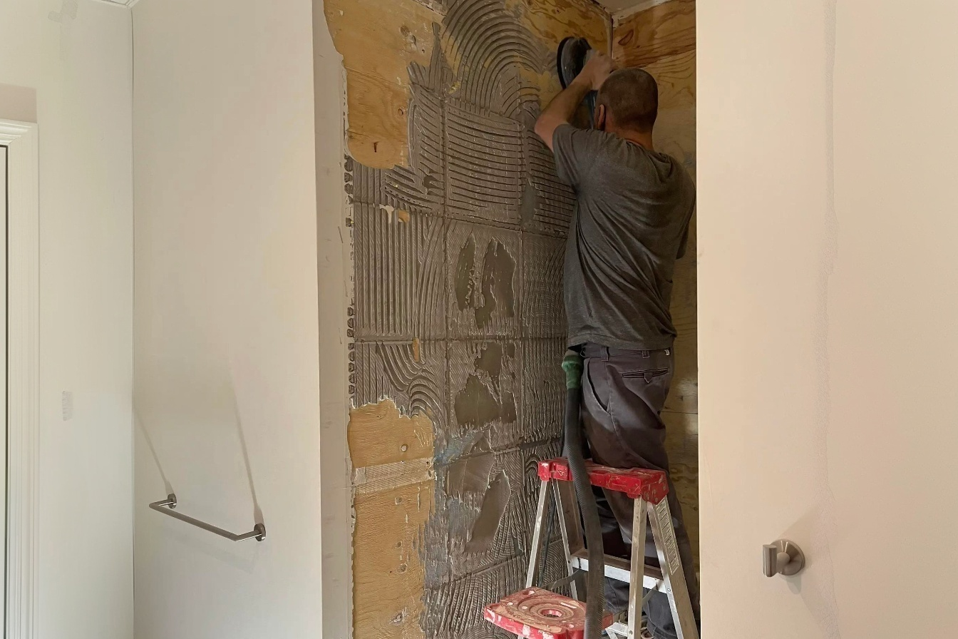 Installation de carrelage mural avec application de mortier-colle sur panneau de douche lors de rénovation de salle de bain