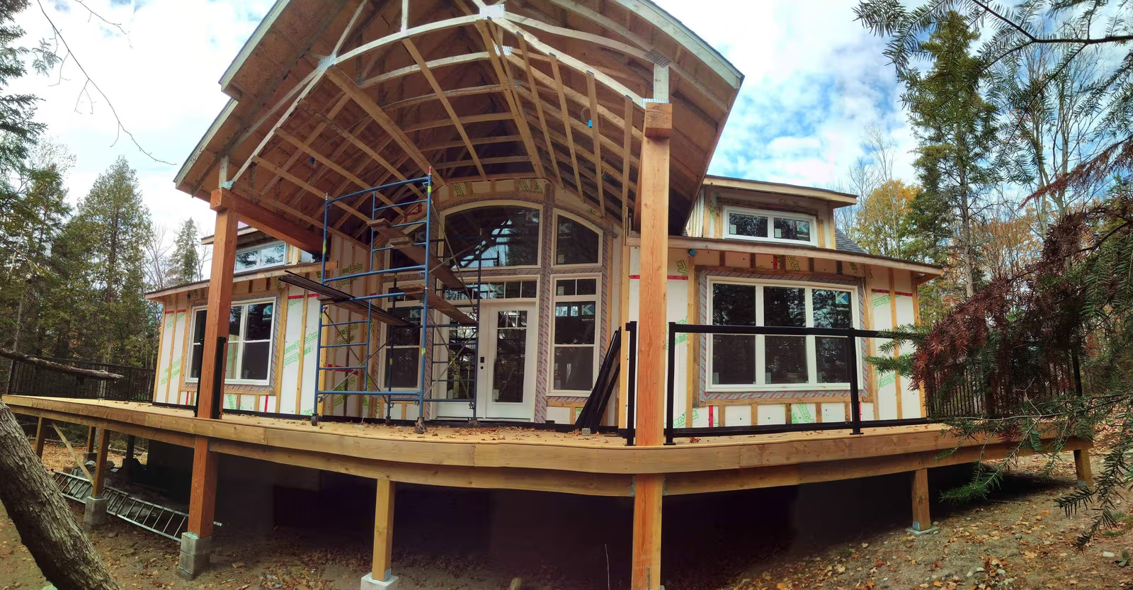 Maison en construction avec charpente apparente, grande terrasse en bois surélevée et échafaudage à l’avant /&nbsp;House under construction with exposed timber framing, large elevated wooden deck and scaffolding at the front