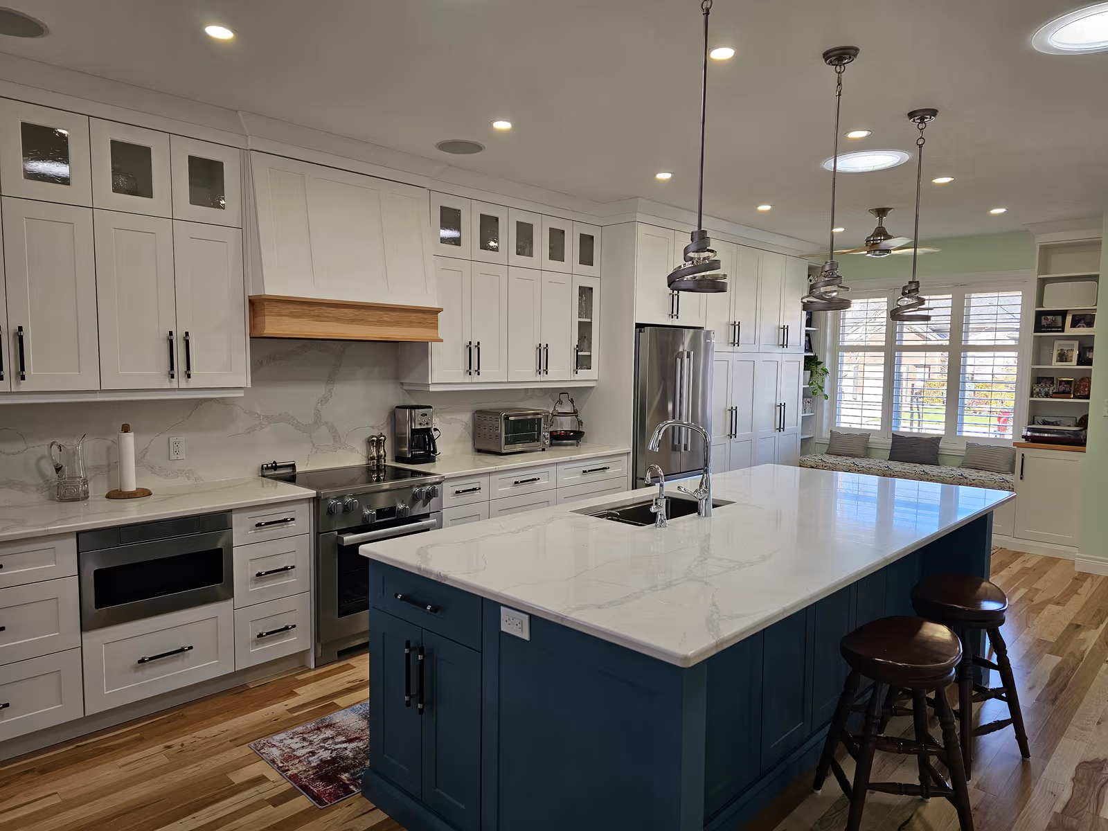 Modern kitchen with large blue central island, white quartz countertop, white cabinets and elegant pendant lighting