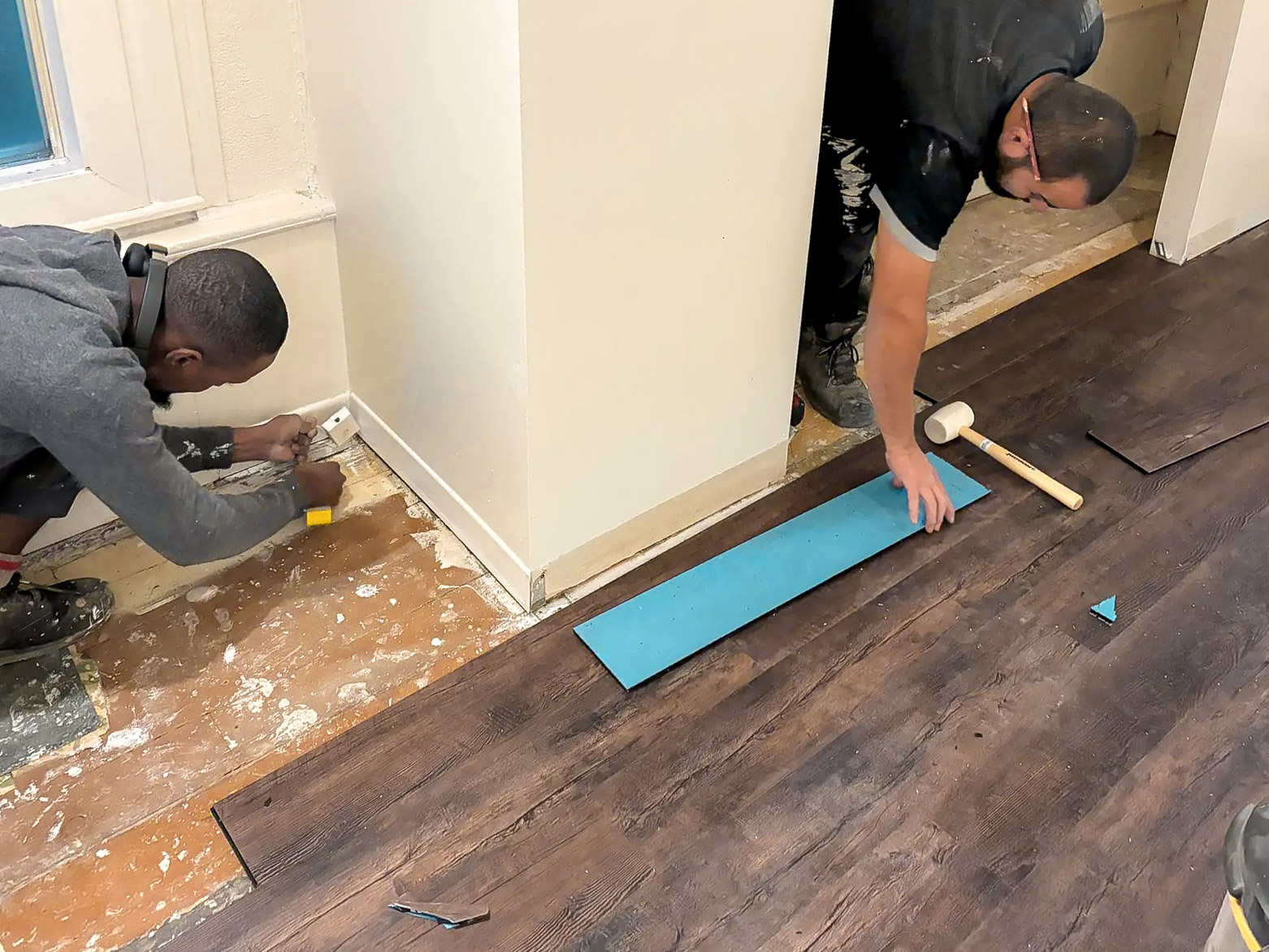 Installation de plancher stratifié par deux ouvriers dans une pièce résidentielle.