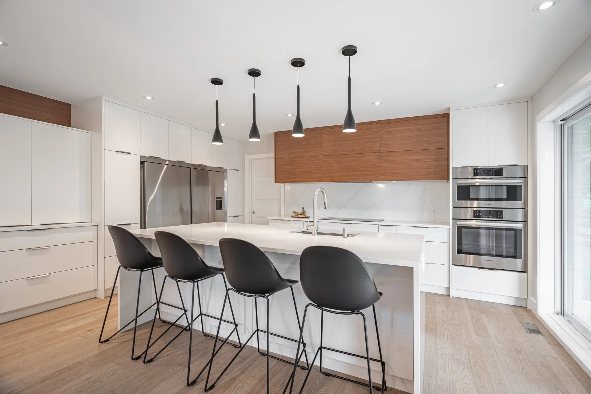 Cuisine moderne avec îlot central blanc, armoires minimalistes blanches et bois, électroménagers en acier inoxydable et luminaires suspendus noirs