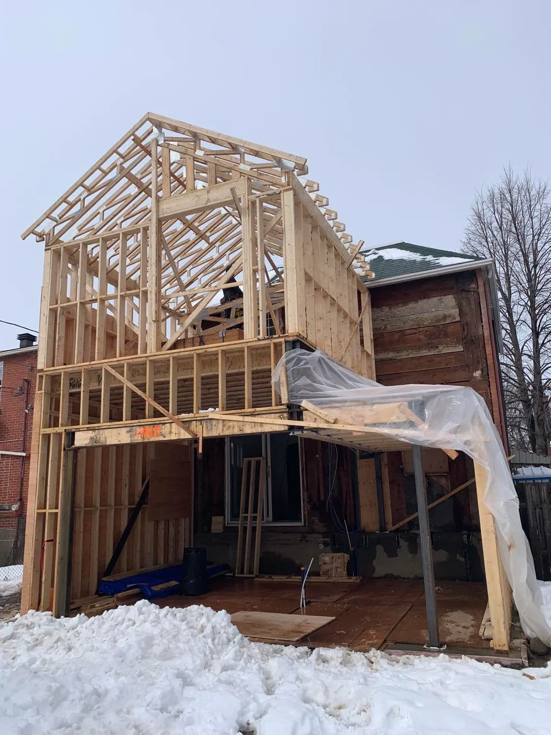 Chantier de construction résidentielle avec agrandissement de maison et ossature en bois en hiver.