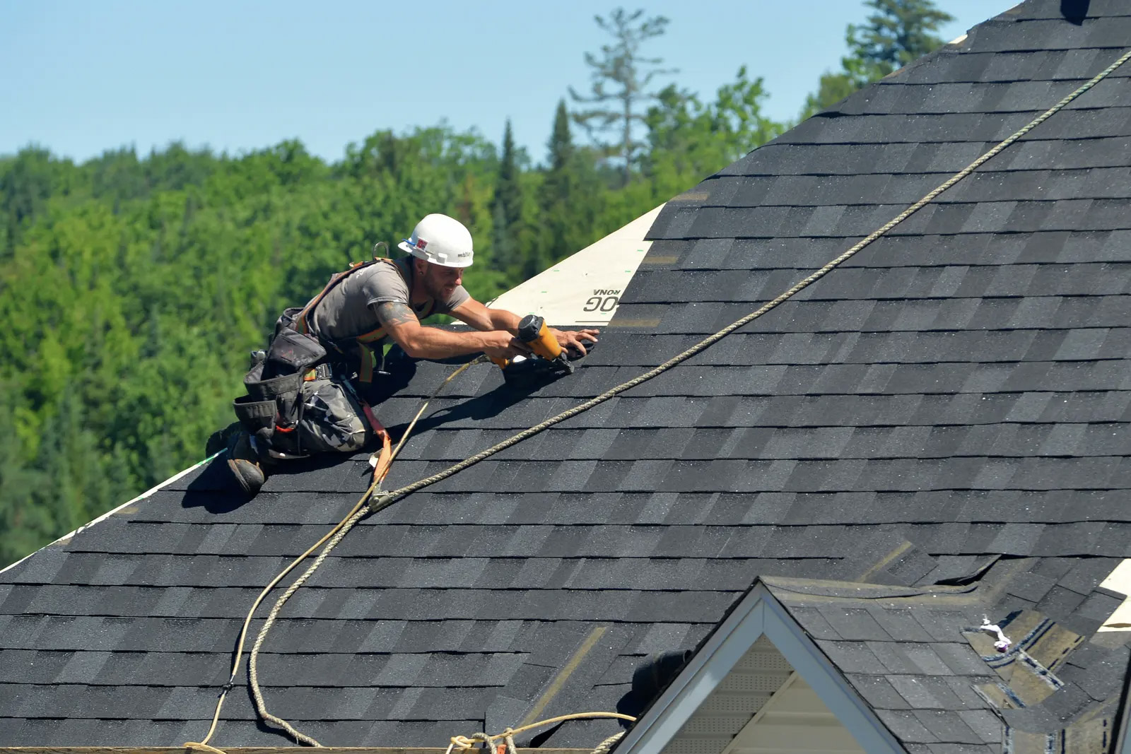 Ouvrier sur un toit en pente posant des bardeaux d’asphalte avec un pistolet à clous de toiture en plein air