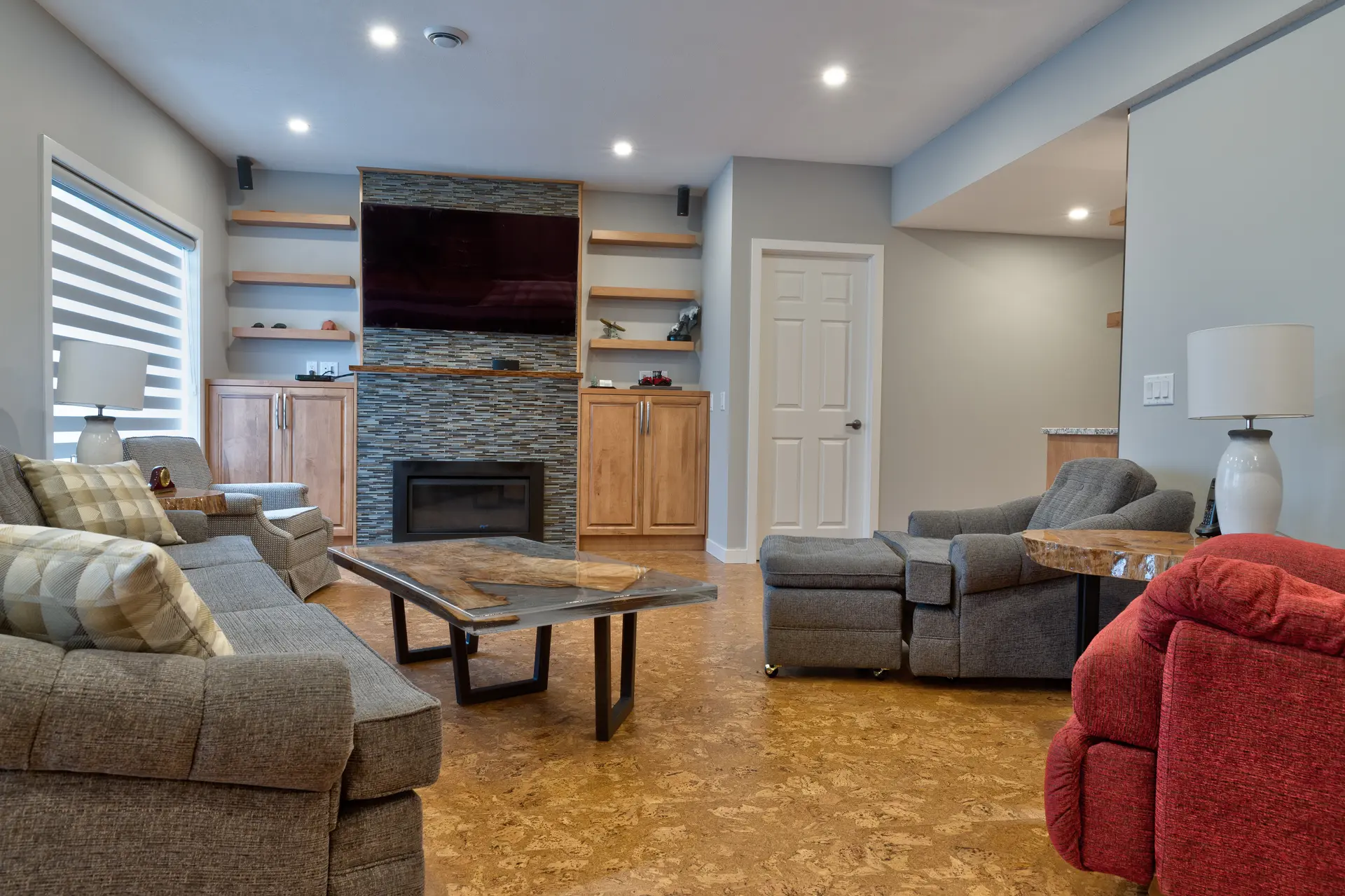 Modern living room with cork flooring, stone fireplace, wall-mounted TV and comfortable seating in a finished basement