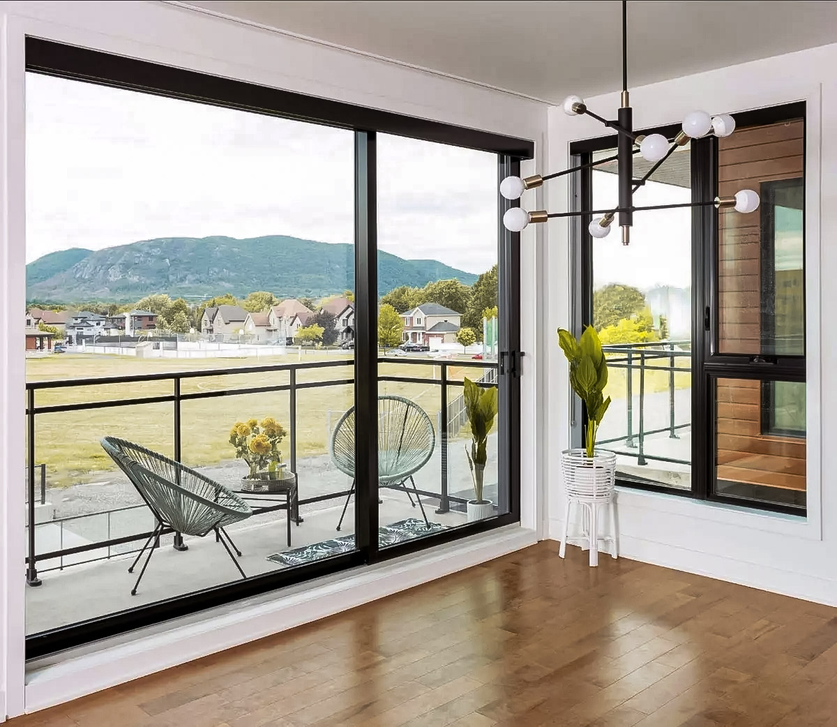 Intérieur lumineux avec grandes portes patio vitrées, balcon moderne, plancher en bois et vue sur les montagnes.