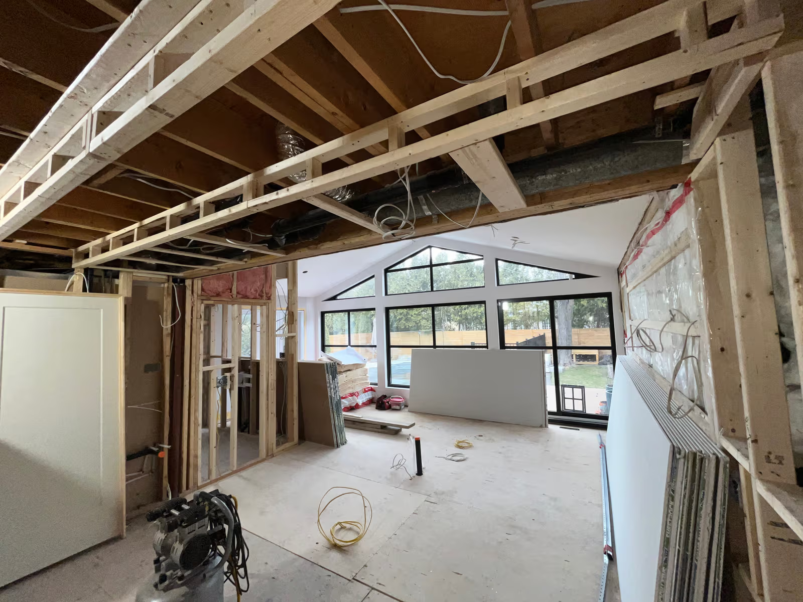 Intérieur de maison en rénovation avec charpente apparente, câblage, gypse et grandes fenêtres noires