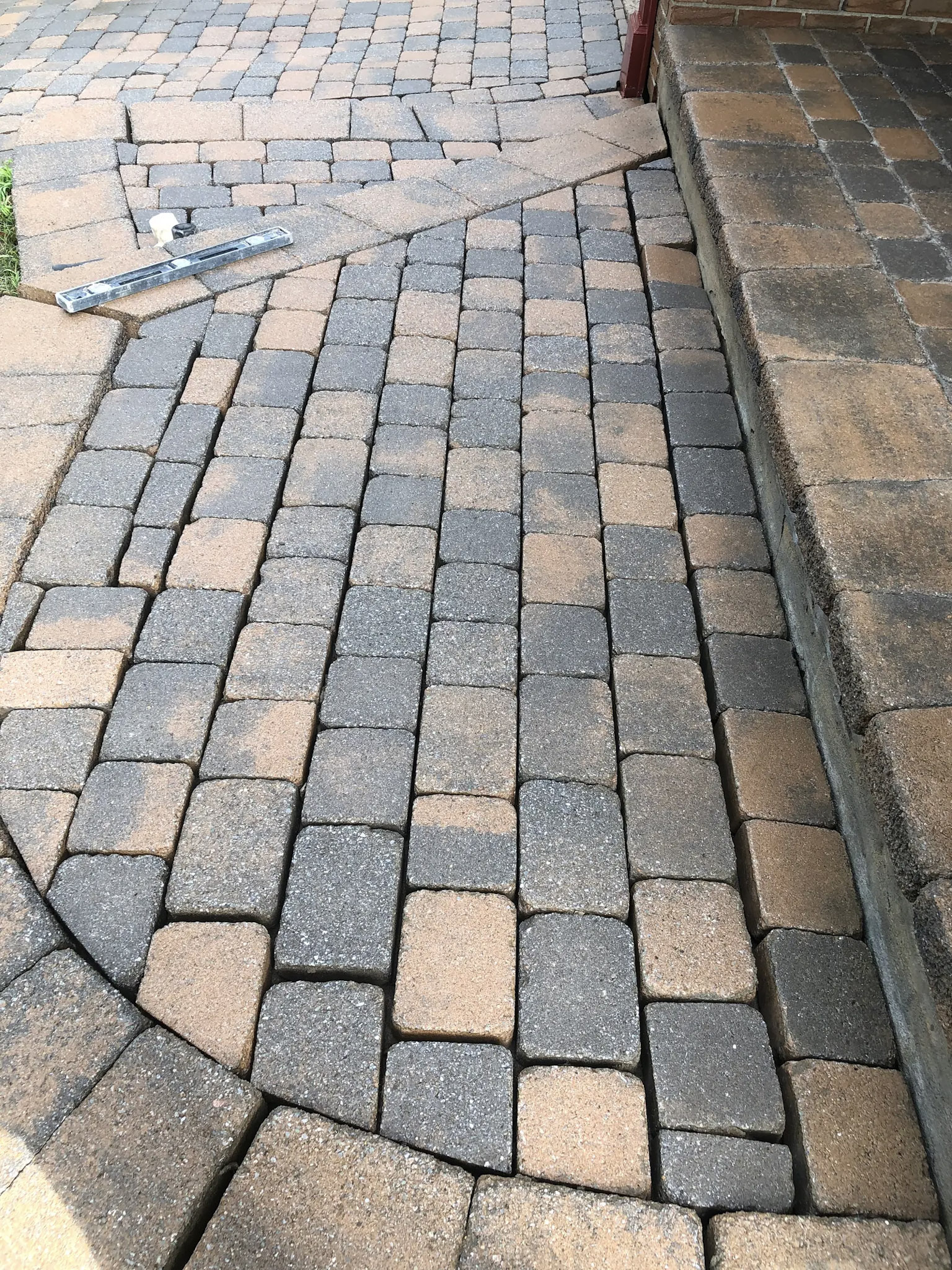 Repair of an interlocking paver driveway with paver realignment and surface leveling beside the steps of a residential front entrance.