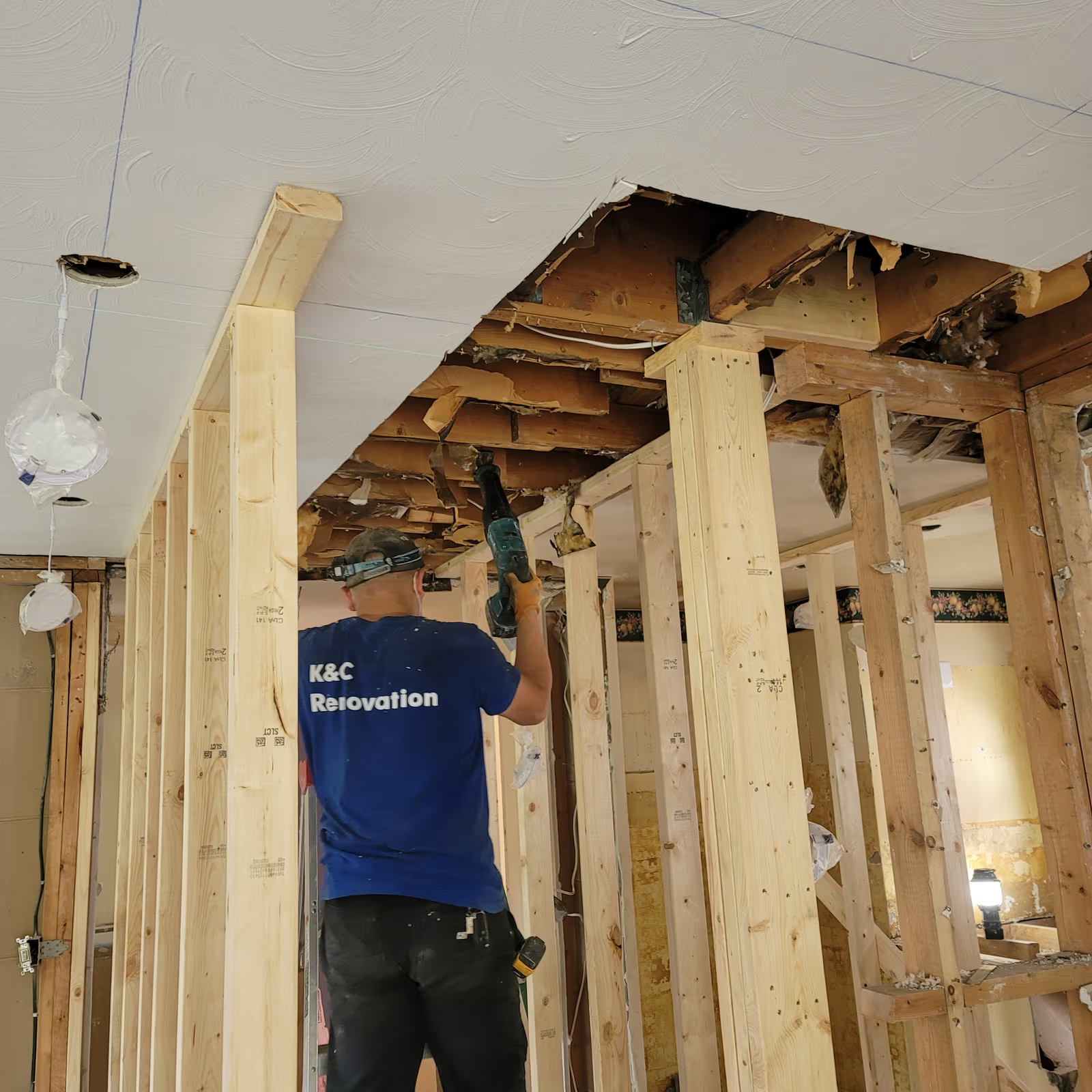 Travailleur rénovant une pièce intérieure avec plafond ouvert, structure de bois apparente et nouvelles divisions en charpente.