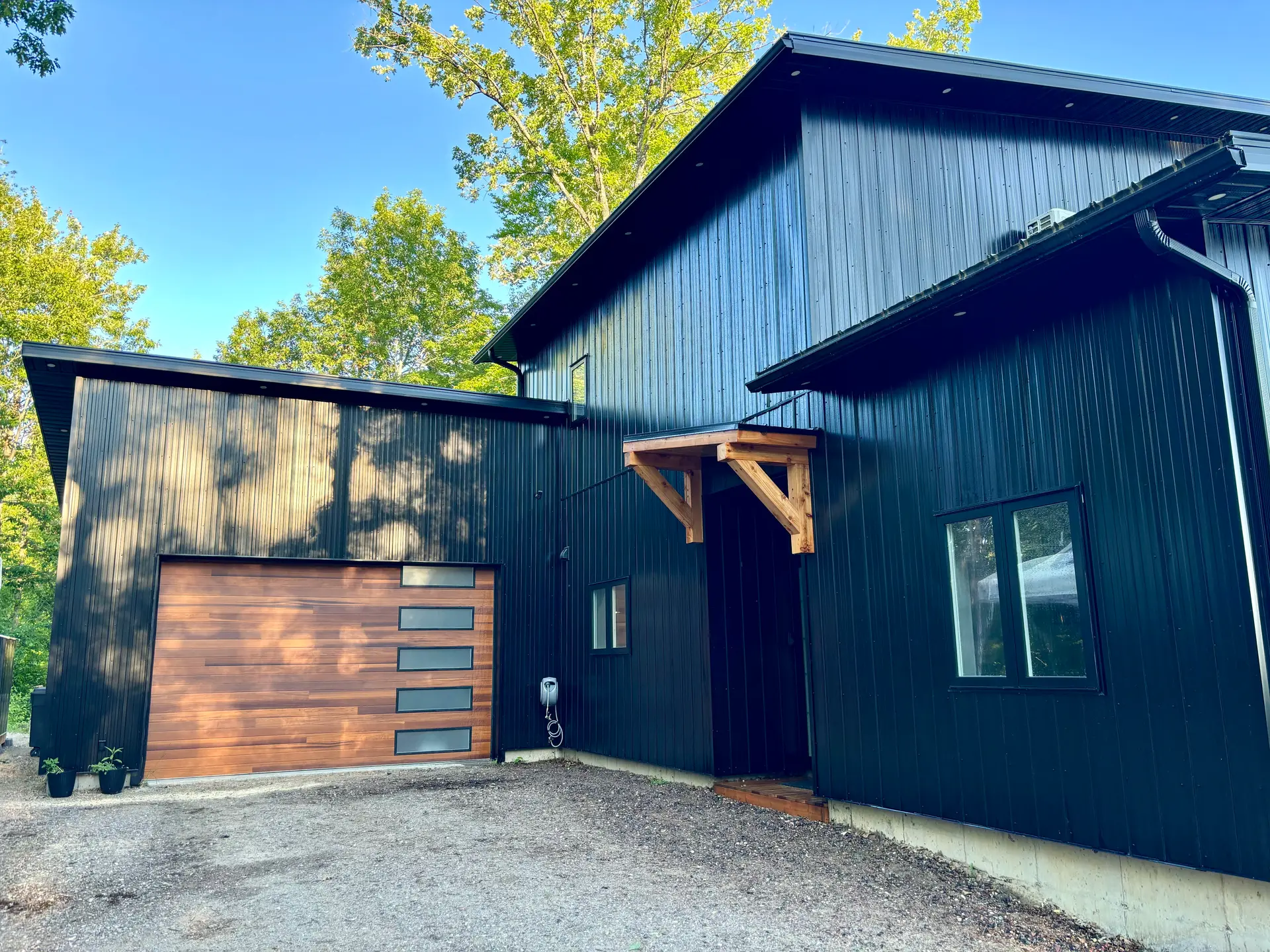 Modern house with vertical black exterior siding, wood-panelled garage with built-in windows, and wooden awning