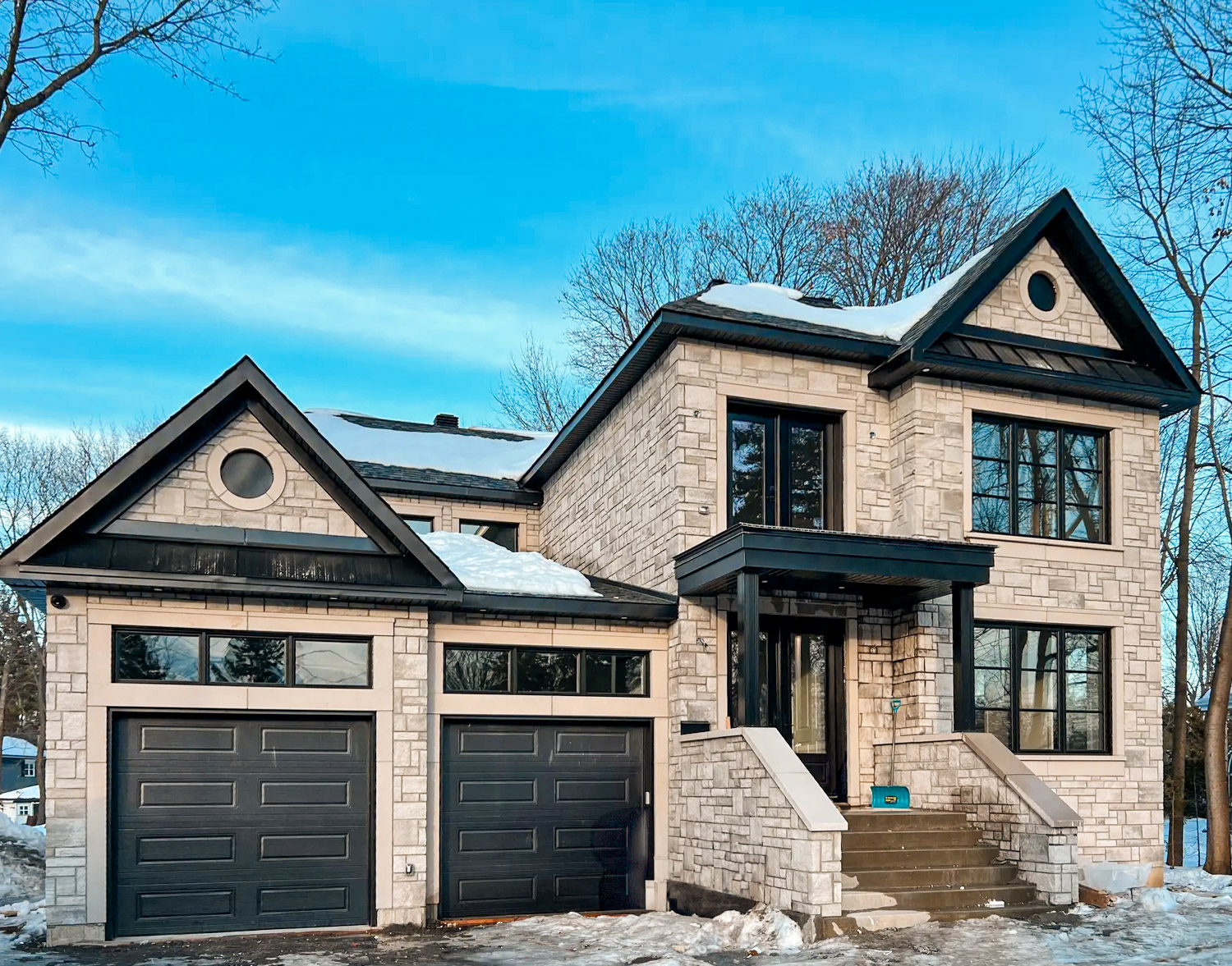 Upscale stone house with two black garages, large windows and snow-covered roof in winter