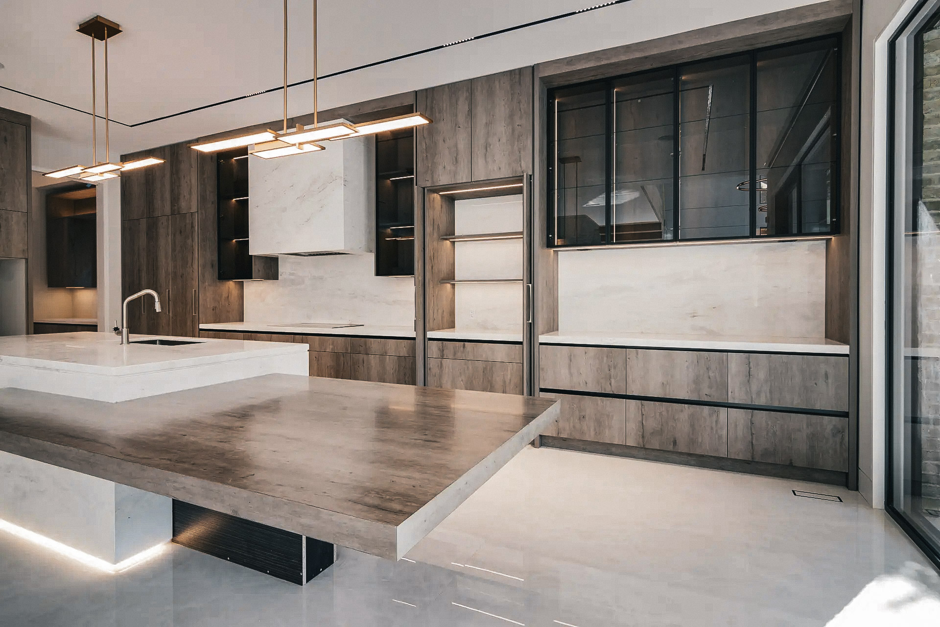 Luxury modern kitchen with large marble island, wood effect cabinets, black glass cabinets and pendant lighting.