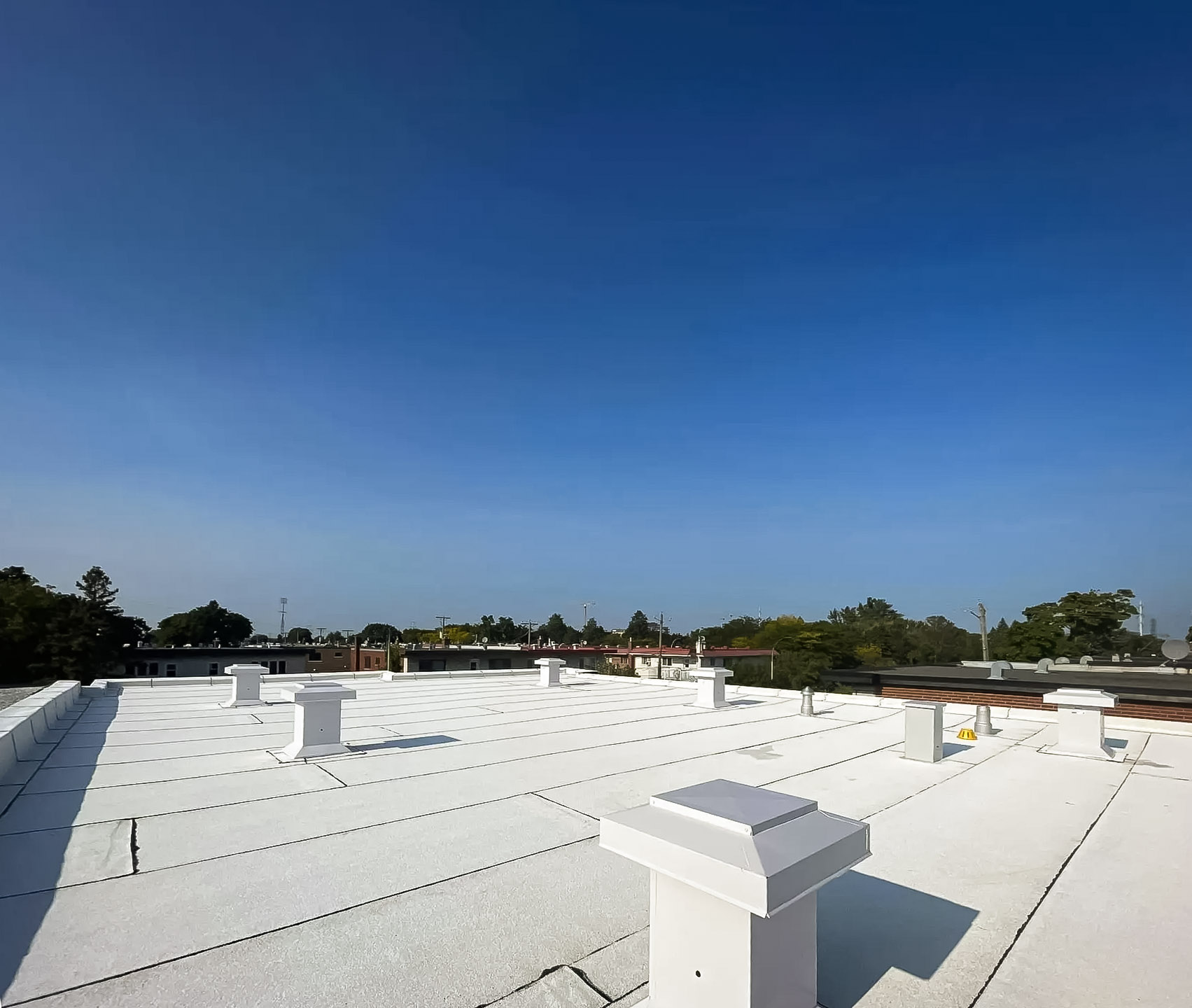 Flat roof covered with a white membrane with several ventilation vents under a clear sky.