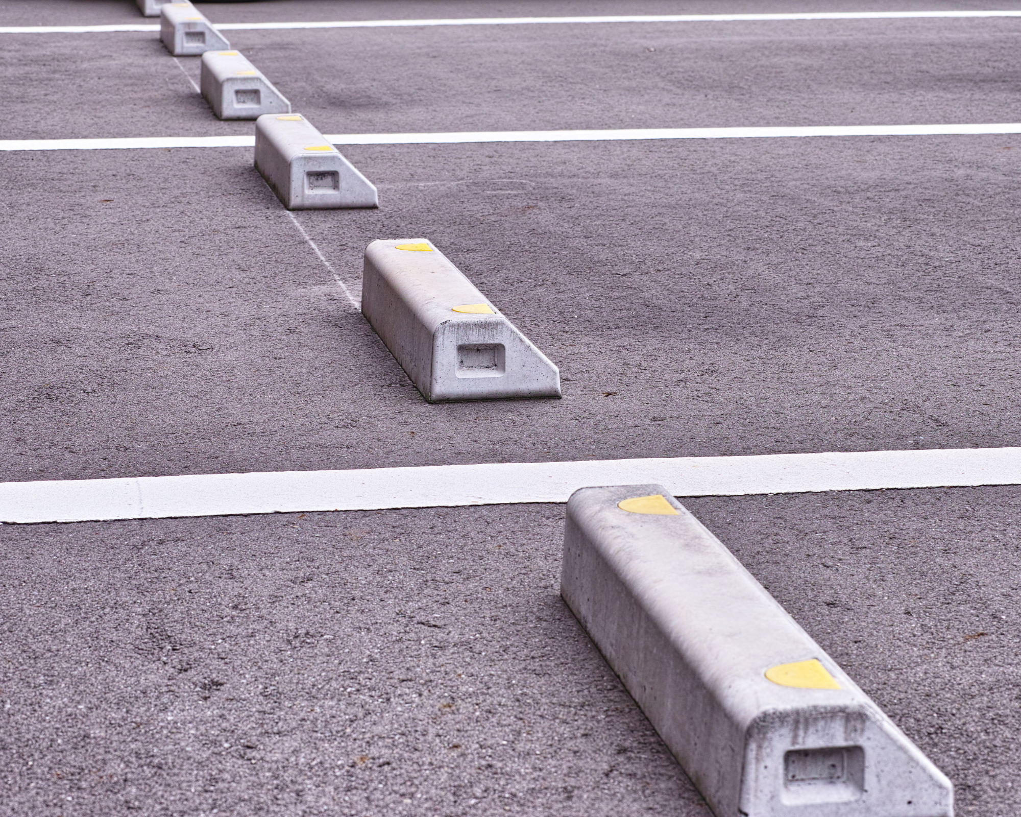 Row of concrete parking stops with yellow markings in an empty parking lot.