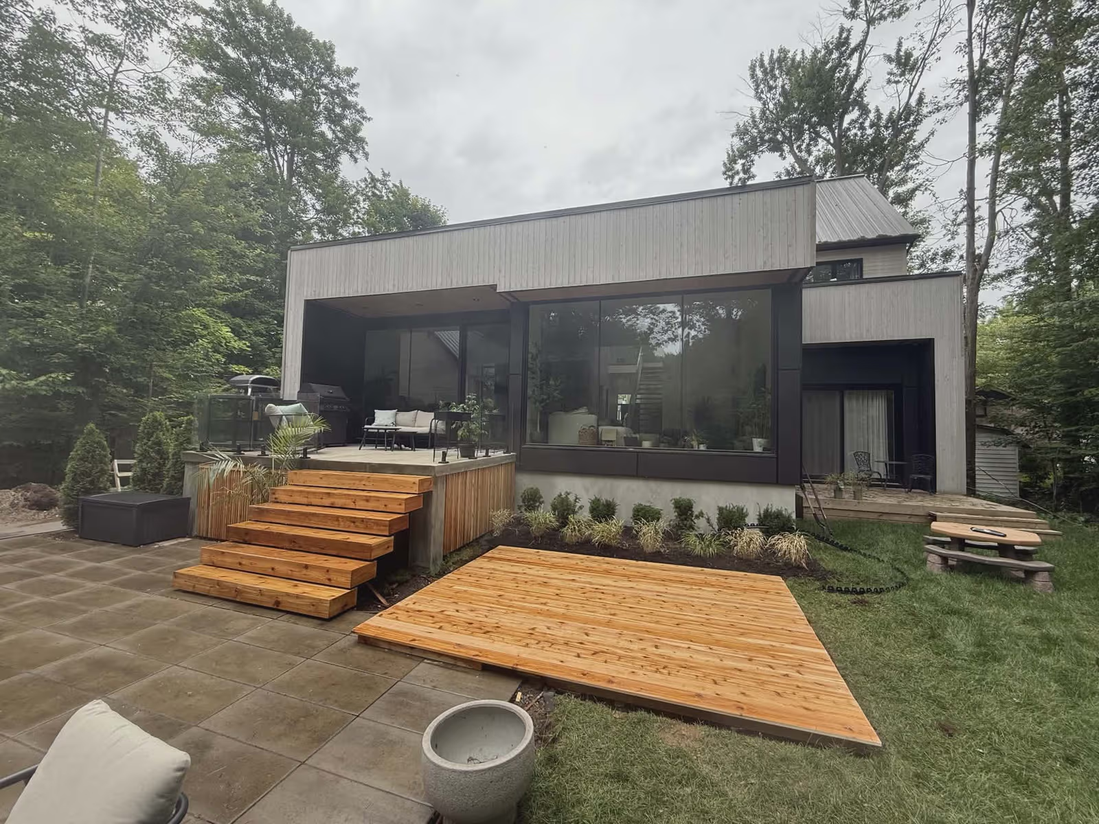 Maison moderne en forêt avec grandes fenêtres, terrasse, escalier en bois et aménagement paysager contemporain