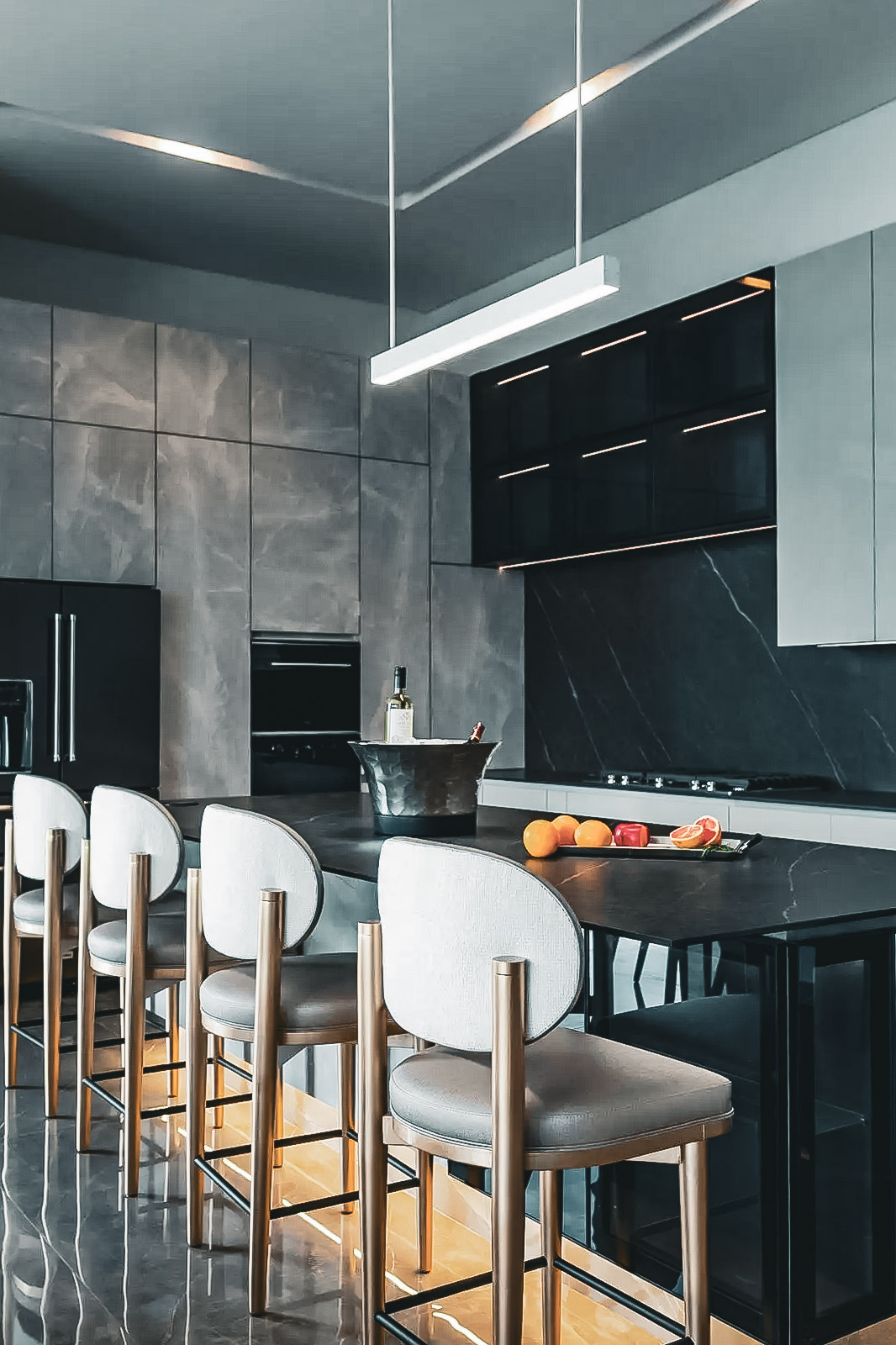 Cuisine moderne haut de gamme avec îlot noir, armoires grises, dosseret marbré et chaises rembourrées.