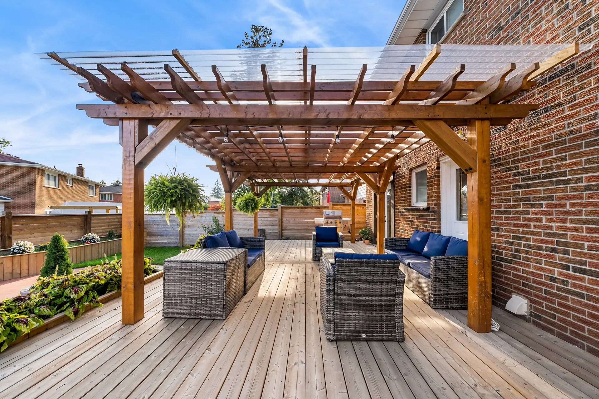 Terrasse extérieure moderne avec pergola en bois, mobilier en rotin, coussins bleus, panneaux d'intimité et aménagement paysager élégant.