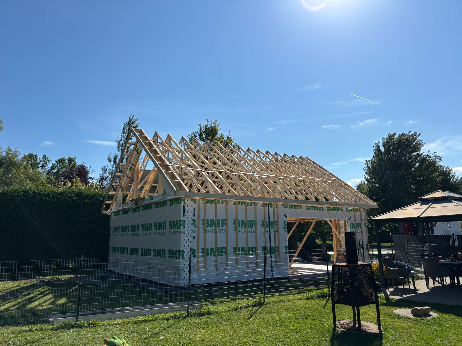 Garage structure under construction with wooden roof framing and partially built walls on residential lot