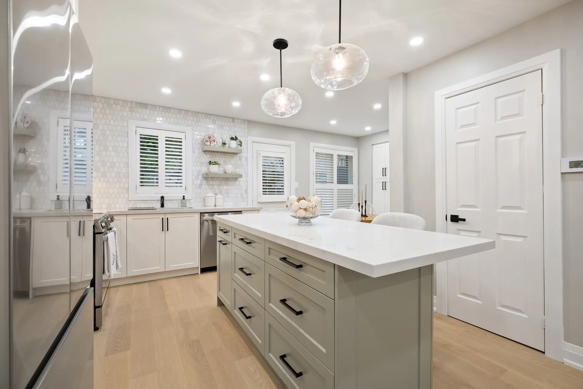 Bright contemporary kitchen with sage green island, white countertops, white hex tile backsplash, and glass pendant lighting.