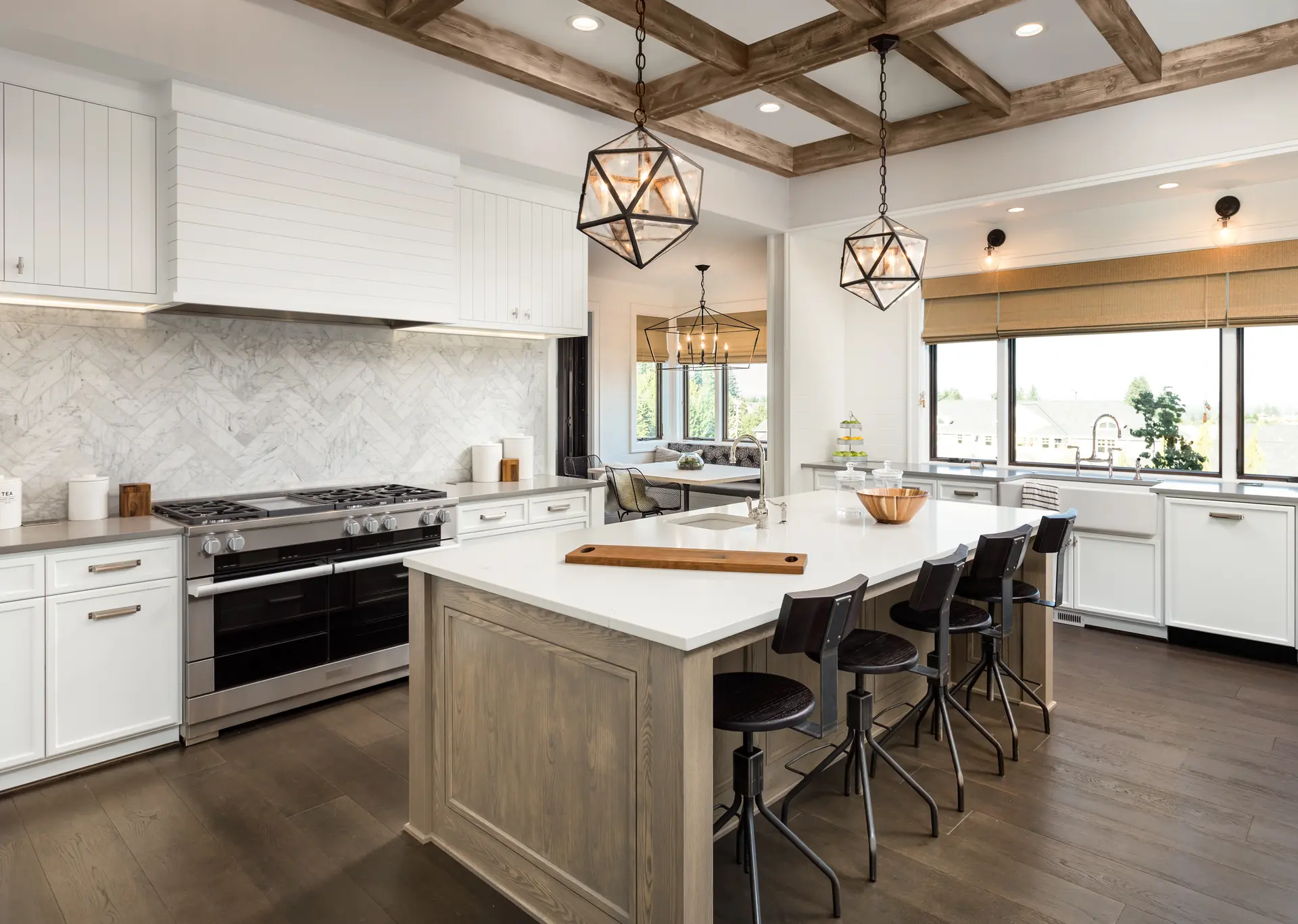 Cuisine moderne spacieuse avec îlot central en bois clair, plan de travail en quartz blanc, plafonds avec poutres apparentes en bois, éclairage suspendu géométrique et grande fenêtre offrant une vue dégagée sur l'extérieur. Décoration élégante avec des tons naturels et un dosseret en marbre.