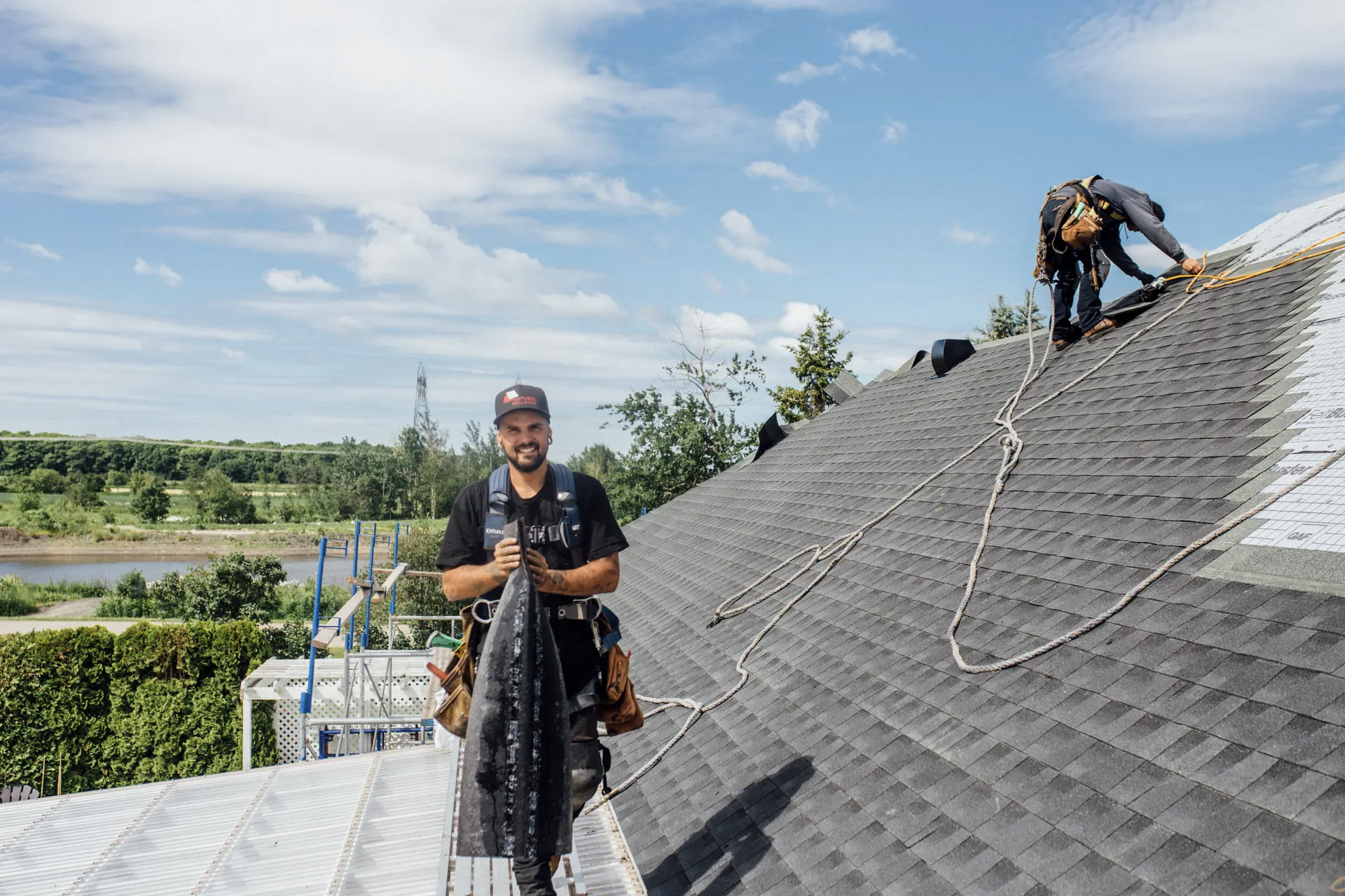 Workers installing a grey shingle roof on a house under a clear sky.