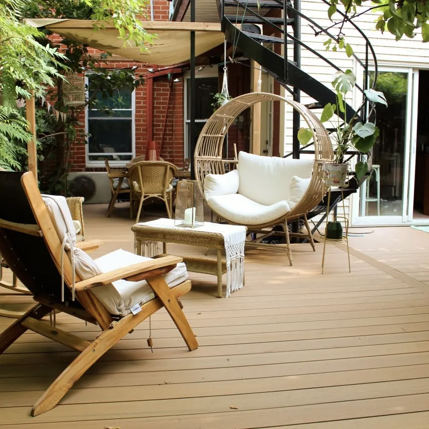 Terrasse en composite avec mobilier en rotin, chaise suspendue, fauteuil en bois et décoration végétale, créant une ambiance chaleureuse et relaxante.