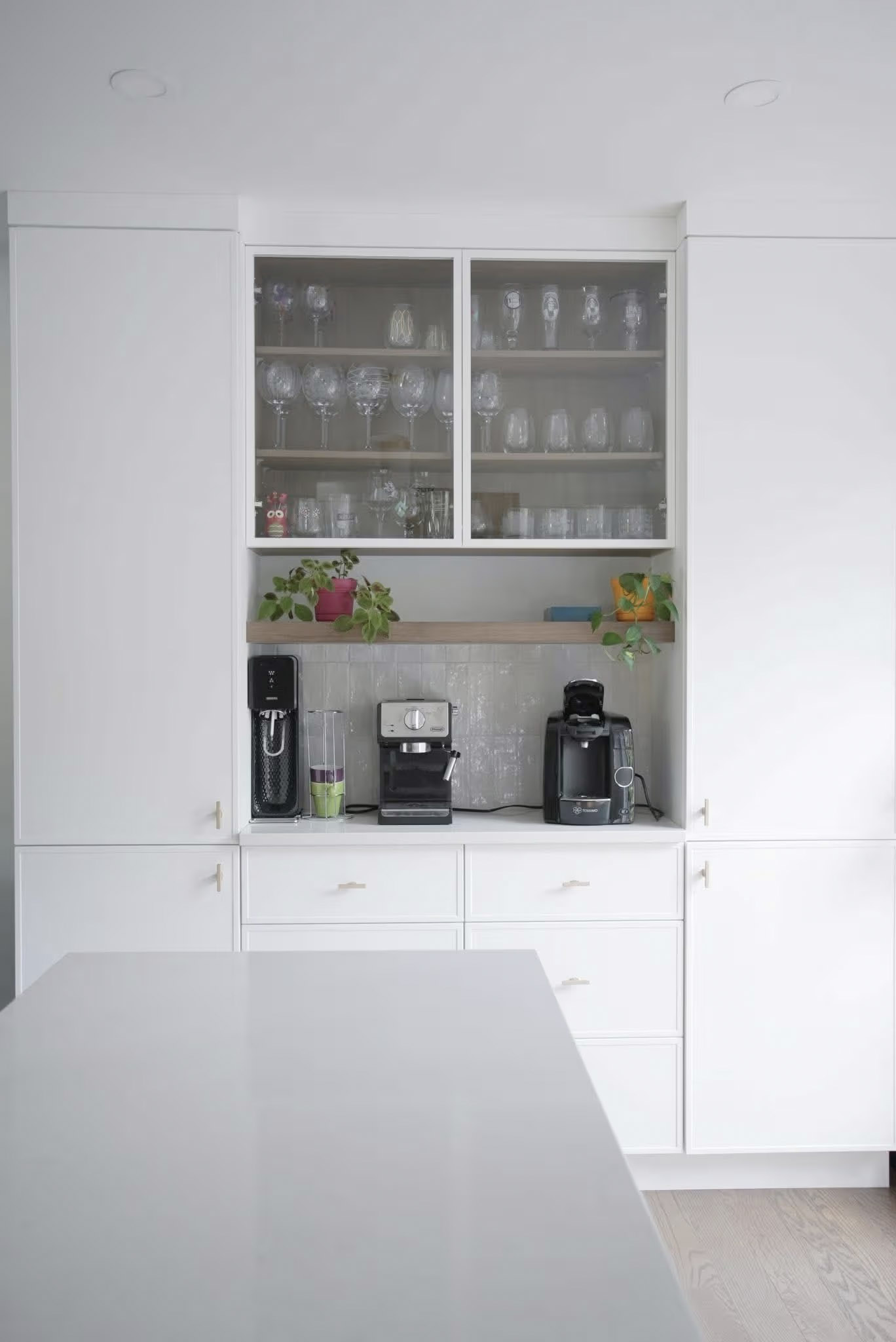 Armoire blanche intégrée avec portes vitrées, rangement pour verres et coin café équipé.