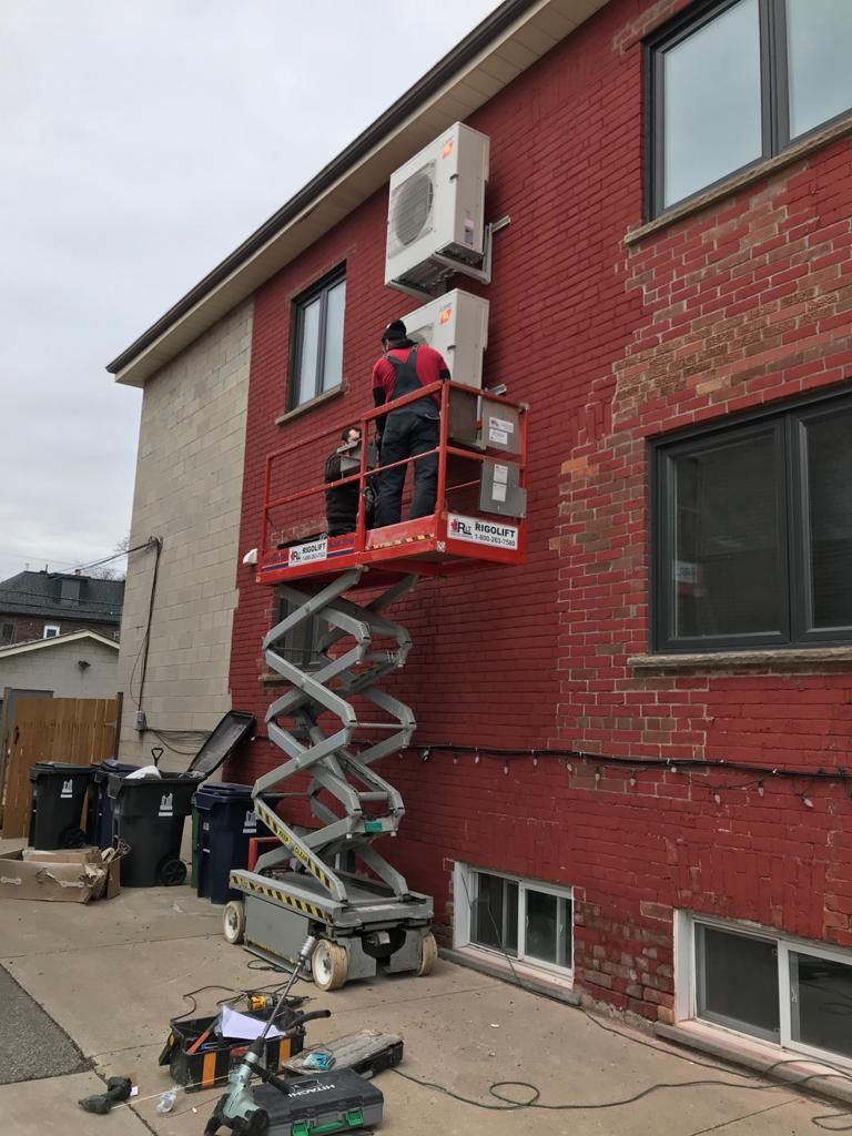 Air conditioning systems installation on an exterior brick wall with HVAC technicians on a lift platform.