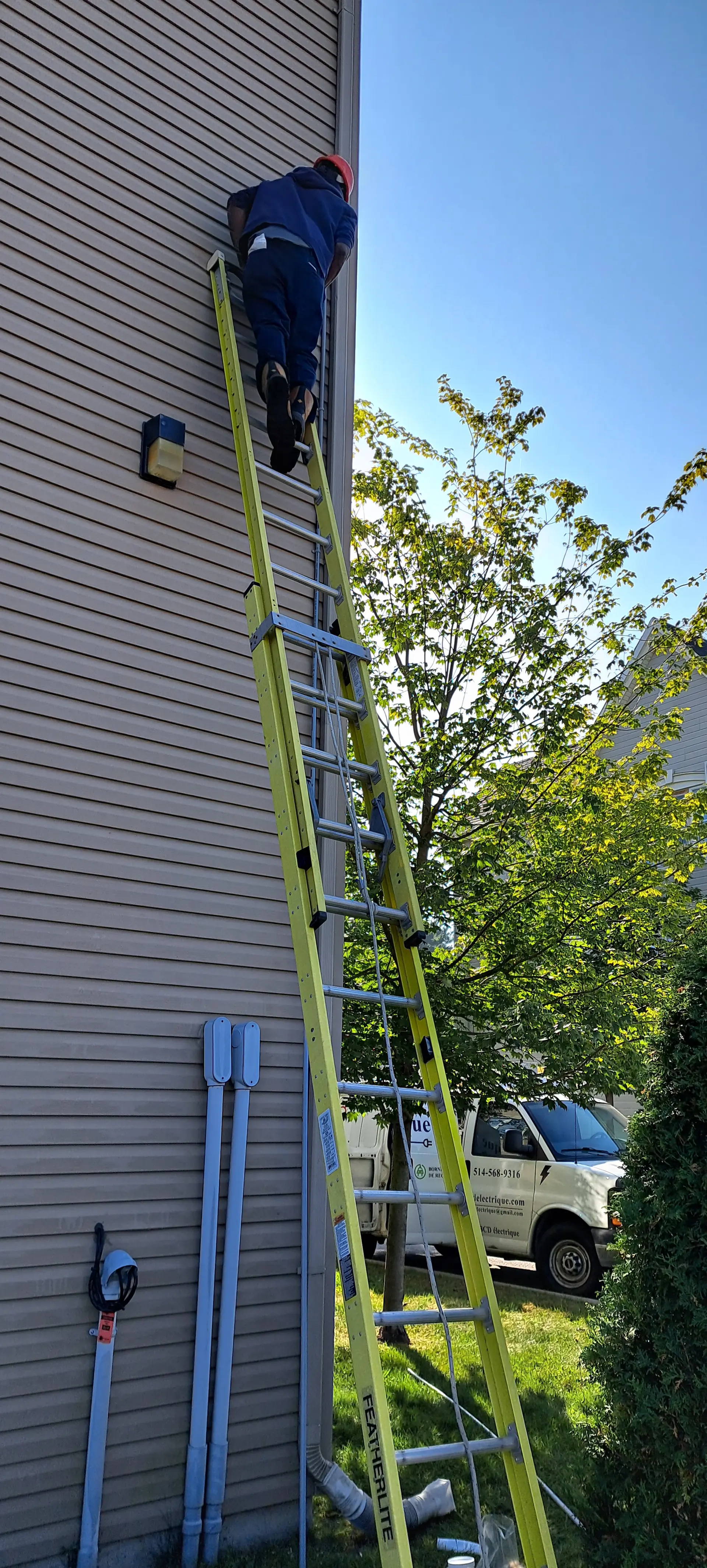 Electrician on a ladder installing or repairing outdoor equipment on the side of a house.