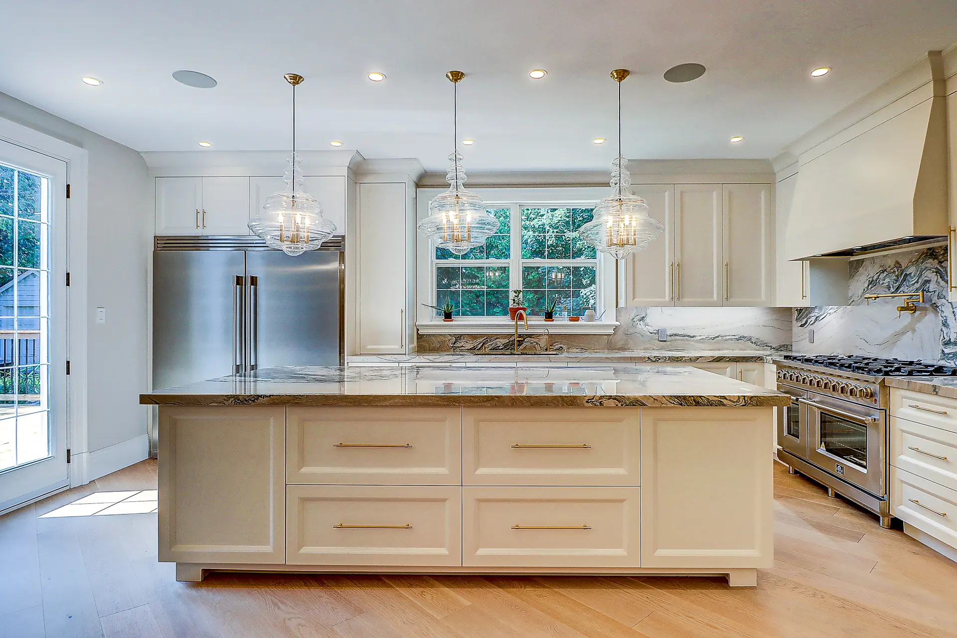 High-end kitchen with large central island, veined marble countertops, stainless steel appliances, and glass pendant lighting.