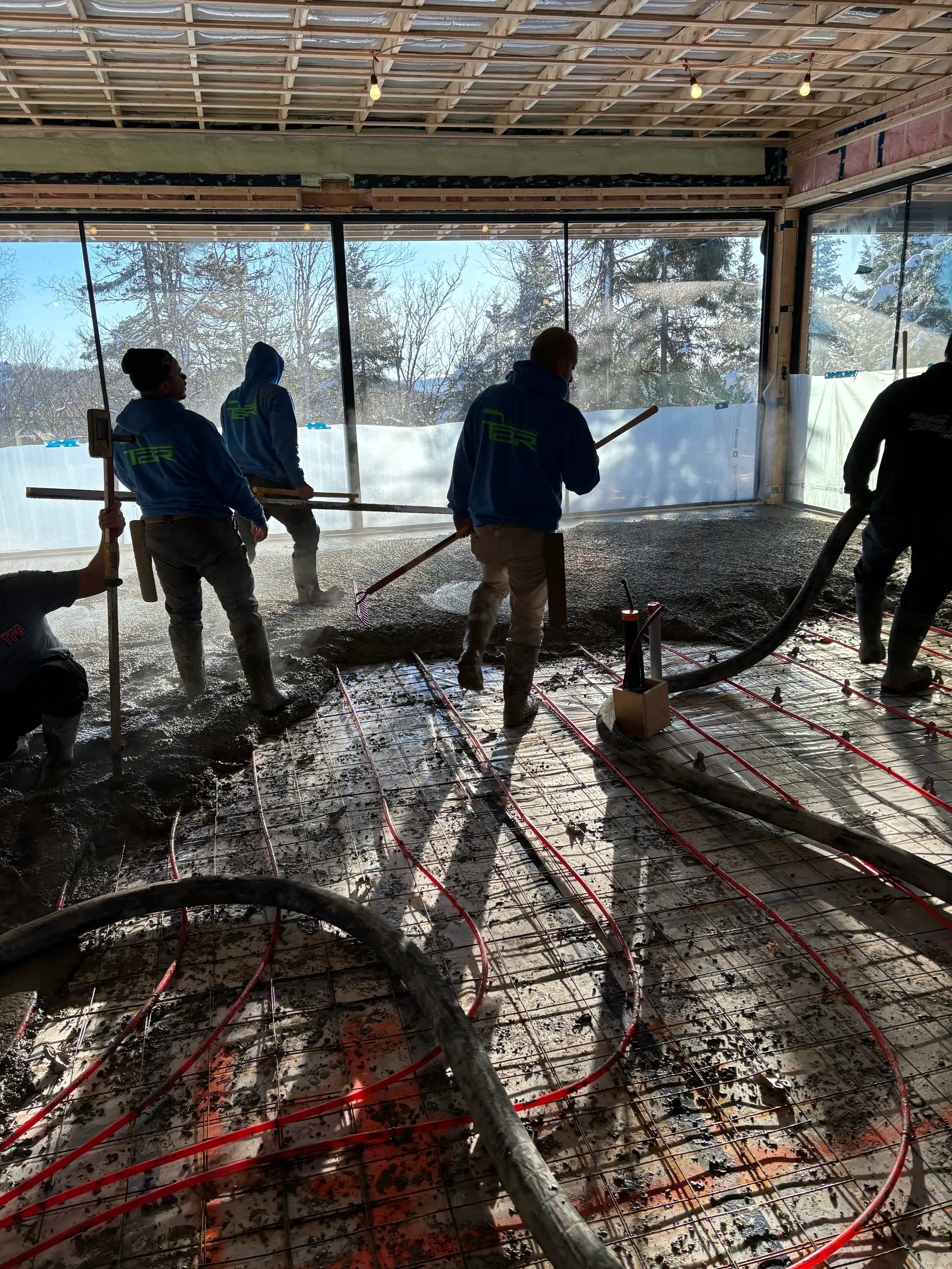 Workers pouring a concrete slab in a building under construction with a visible underfloor heating system.