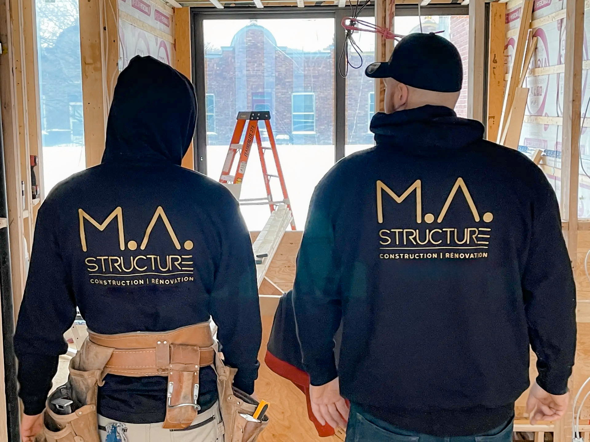 Deux ouvriers de construction portant des chandails à capuchon M.A. Structure dans un chantier en rénovation intérieure boisée