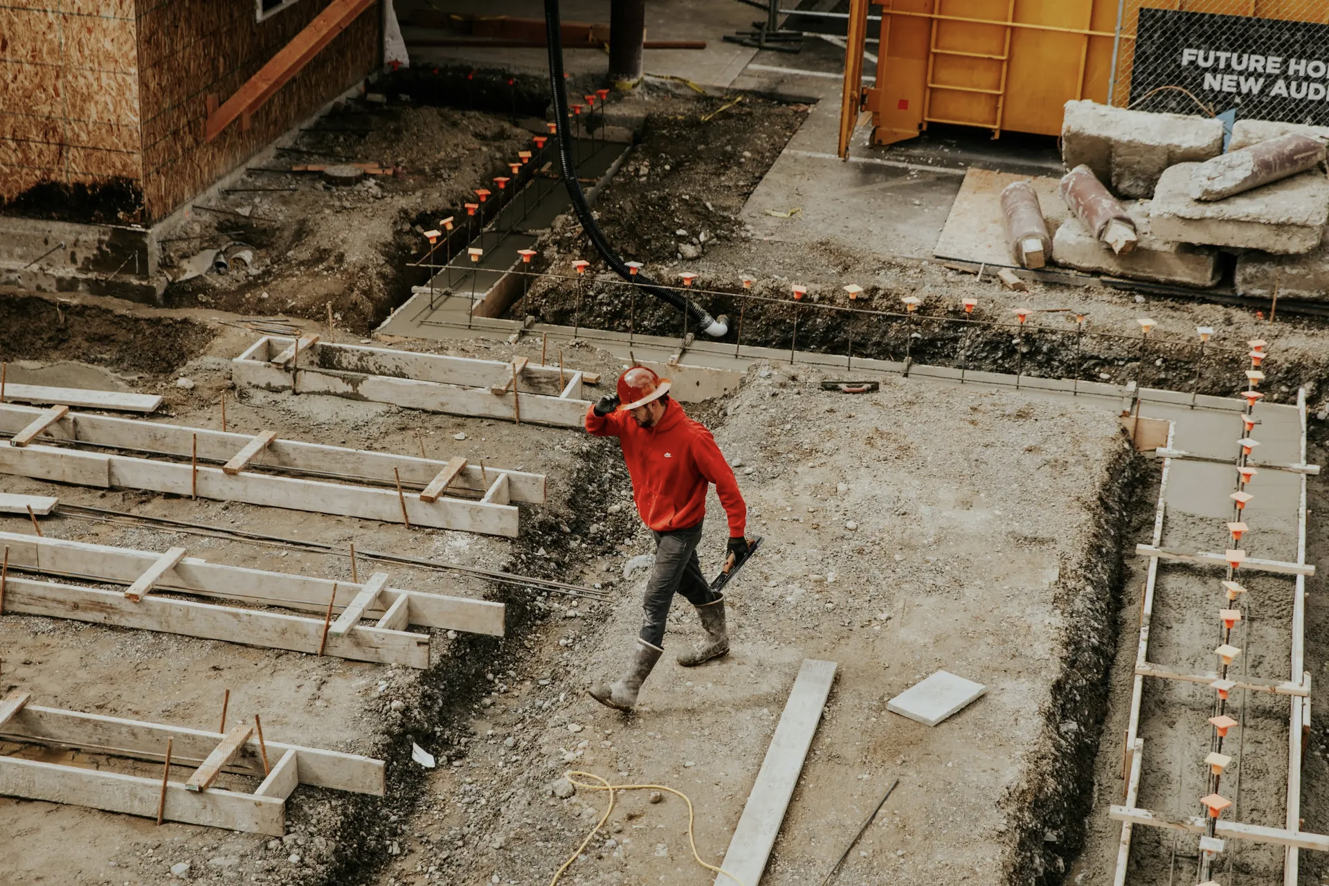 Construction worker walking on a construction site with foundations being laid and wooden frames prepared for concreting.