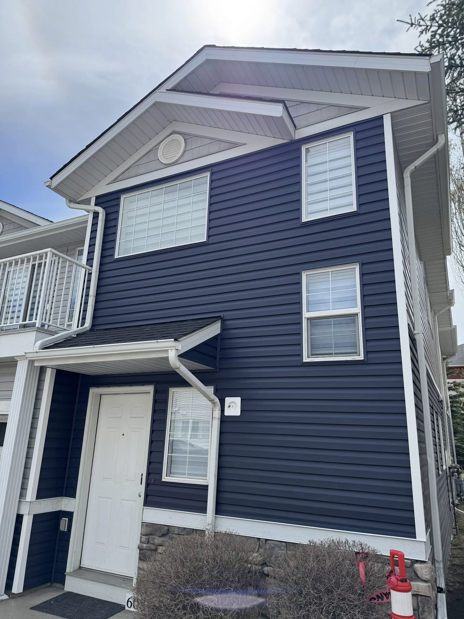 Two-story house facade with dark blue siding, white trim, windows and shingle roof.