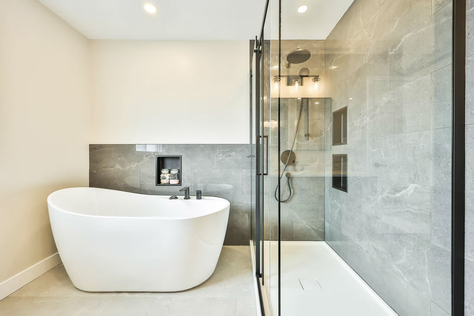 Contemporary bathroom with white freestanding bathtub, glass shower, gray stone effect tiles and black faucets