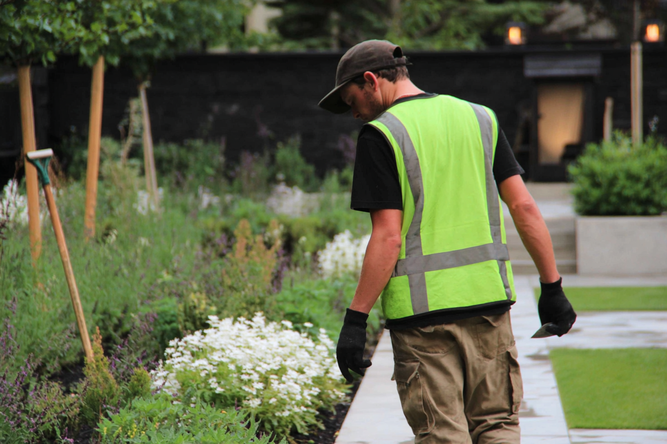 Ouvrier paysagiste inspectant un jardin fleuri avec gilet de sécurité et gants