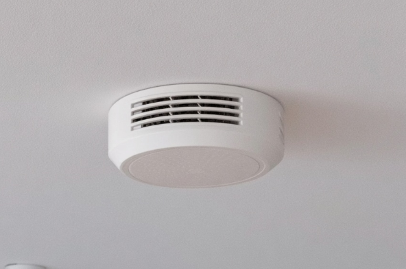 White smoke detector mounted on the ceiling of an interior room for residential safety.