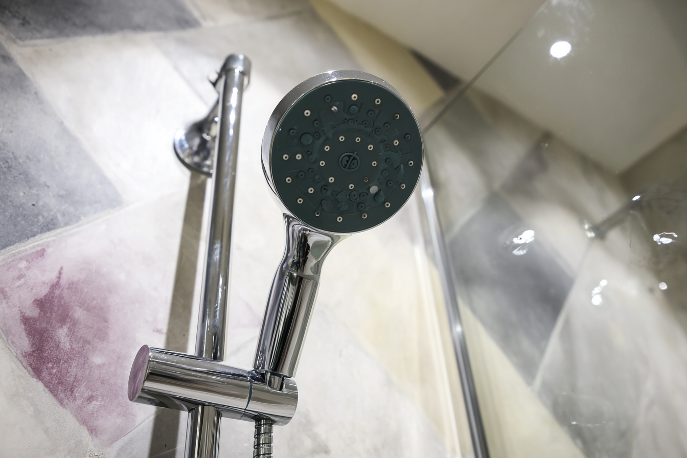 Chrome shower head attached to a wall bar in a modern shower with tiled walls