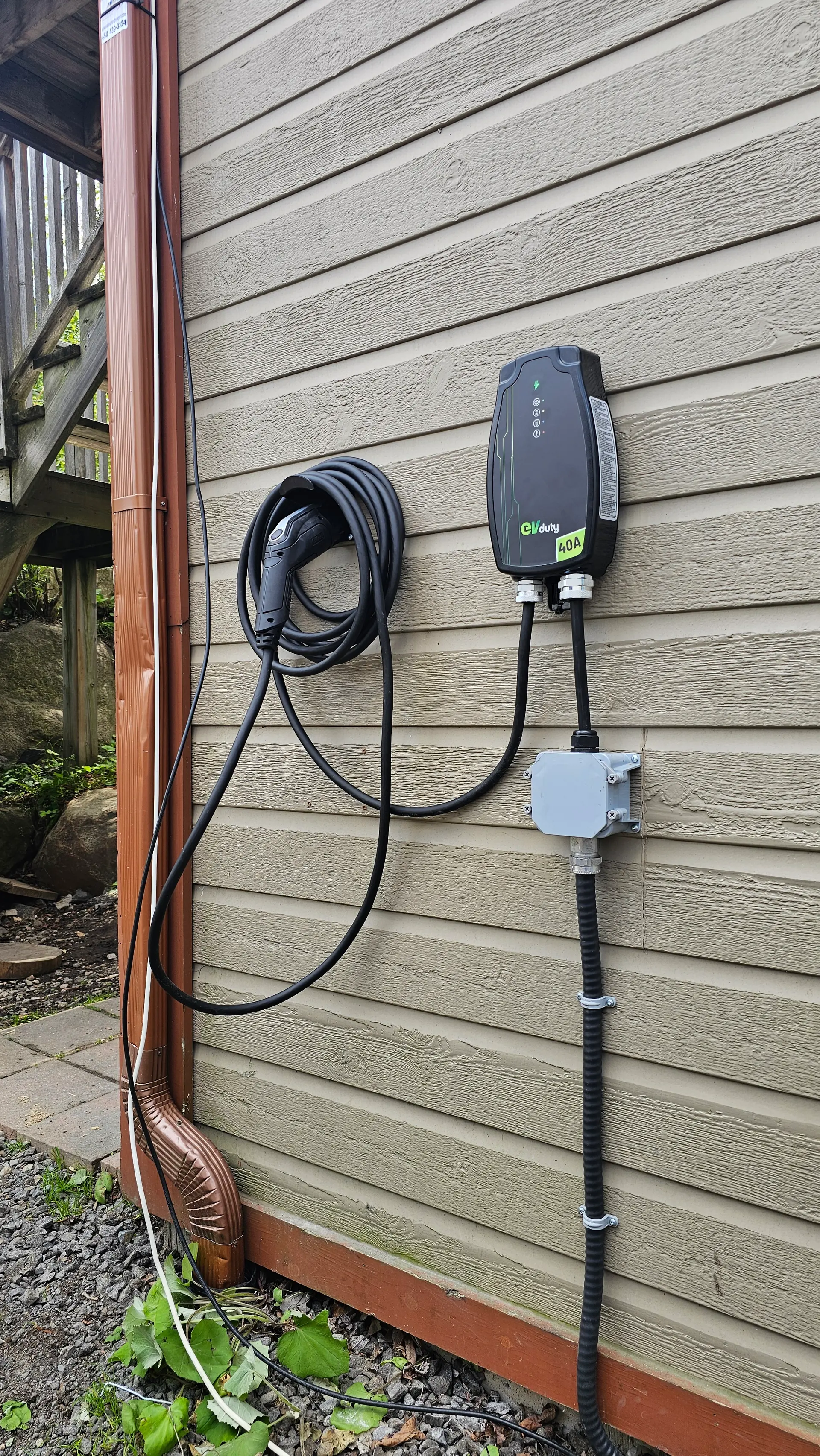 Residential 40-amp electric vehicle charging station installed on beige exterior siding with a coiled cable, junction box, and exposed electrical conduit