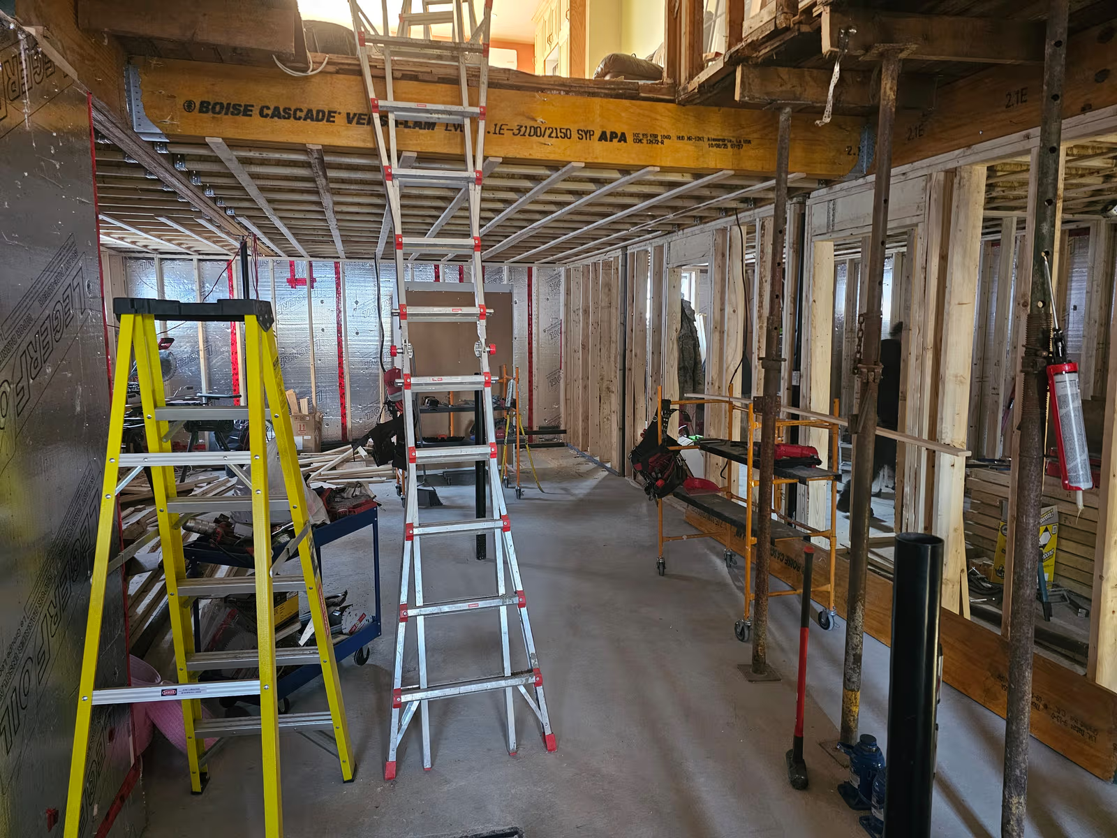 Basement under construction with exposed wood framing, beams, ladders, wall insulation, and construction tools.