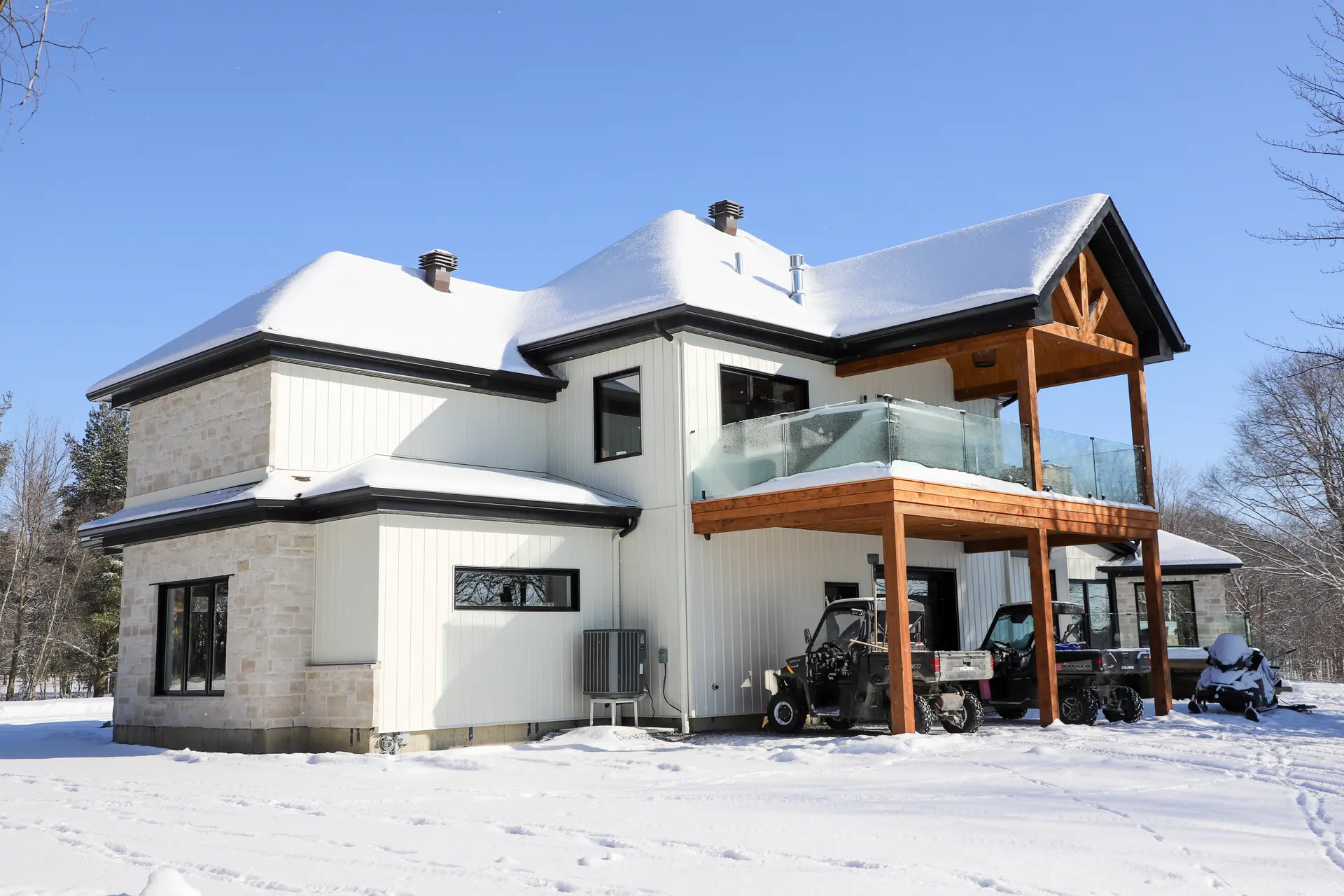 Modern house in winter with white exterior siding, glass balcony, wooden beams, and snow-covered roof
