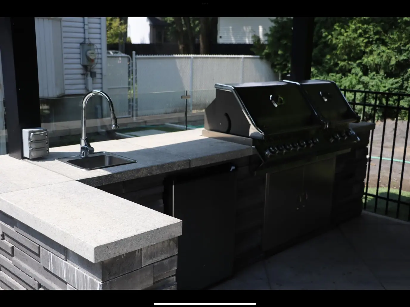 Cuisine extérieure moderne avec barbecue intégré, évier, comptoir en pierre et espace repas couvert