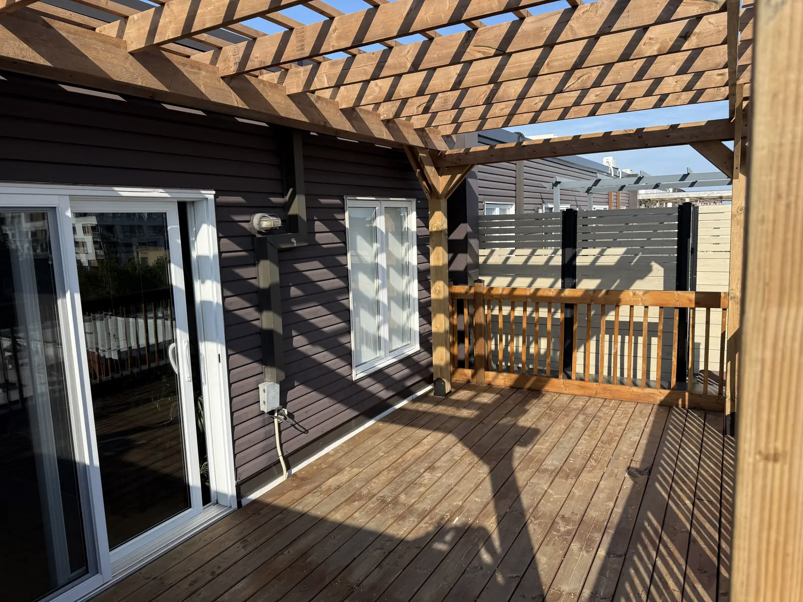 Wooden deck with pergola, railing and sliding patio doors on a residential house.