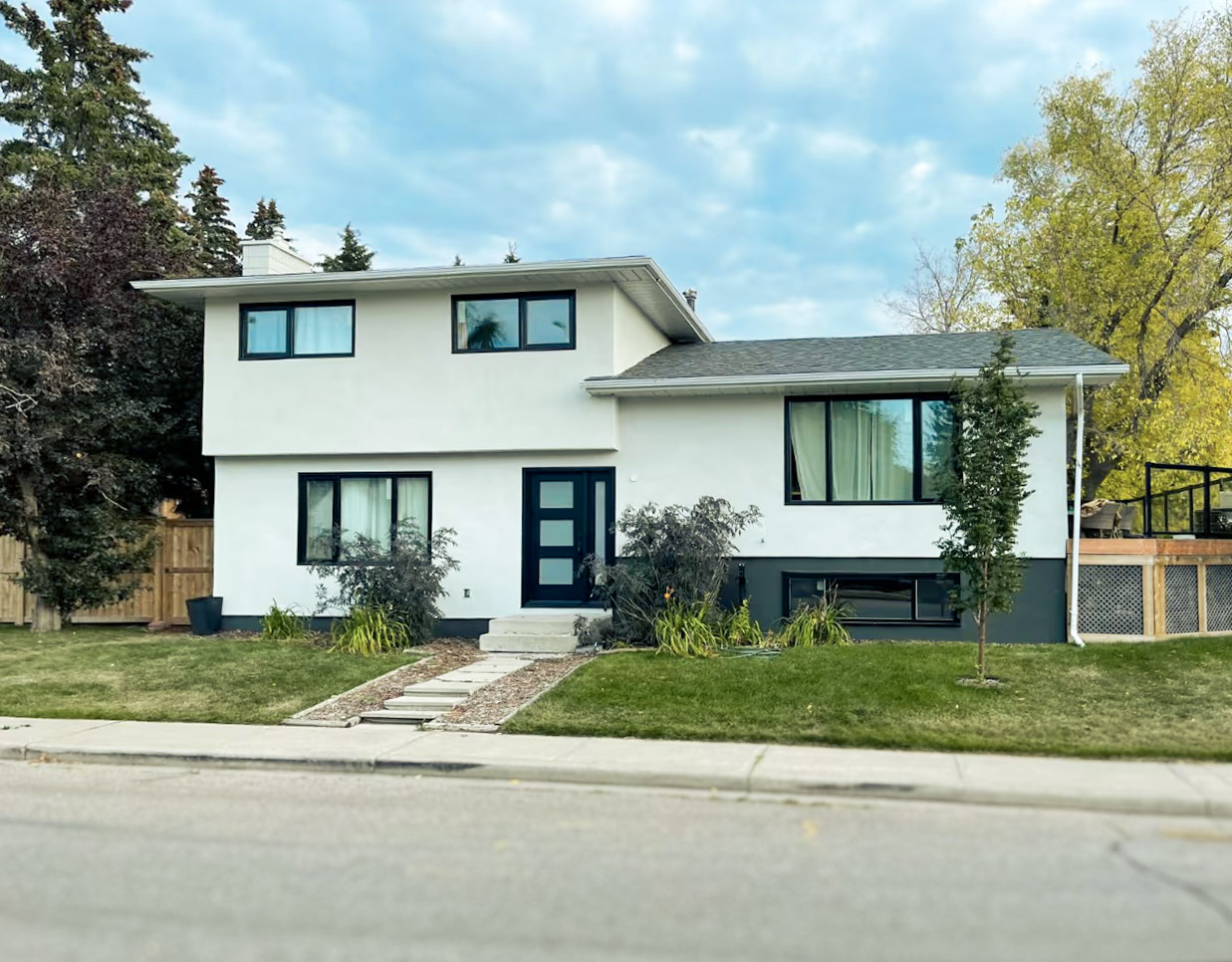 Maison moderne à deux niveaux avec façade blanche, grandes fenêtres noires et aménagement paysager simple en cour avant
